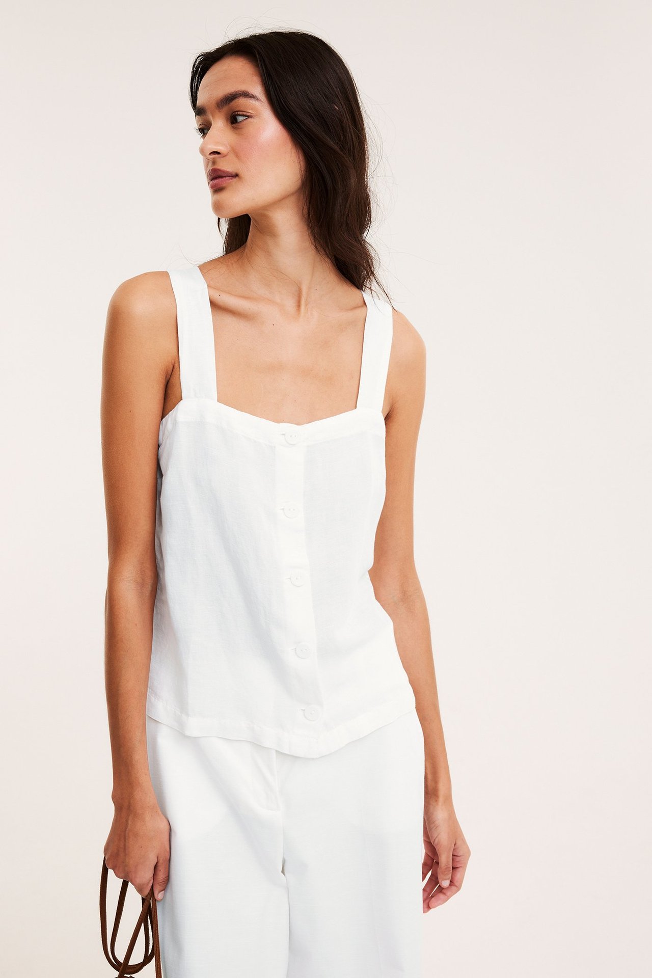 Framifrån: Kvinna i vitt linne i linnemix med breda axelband, knappar fram, och vita byxor.