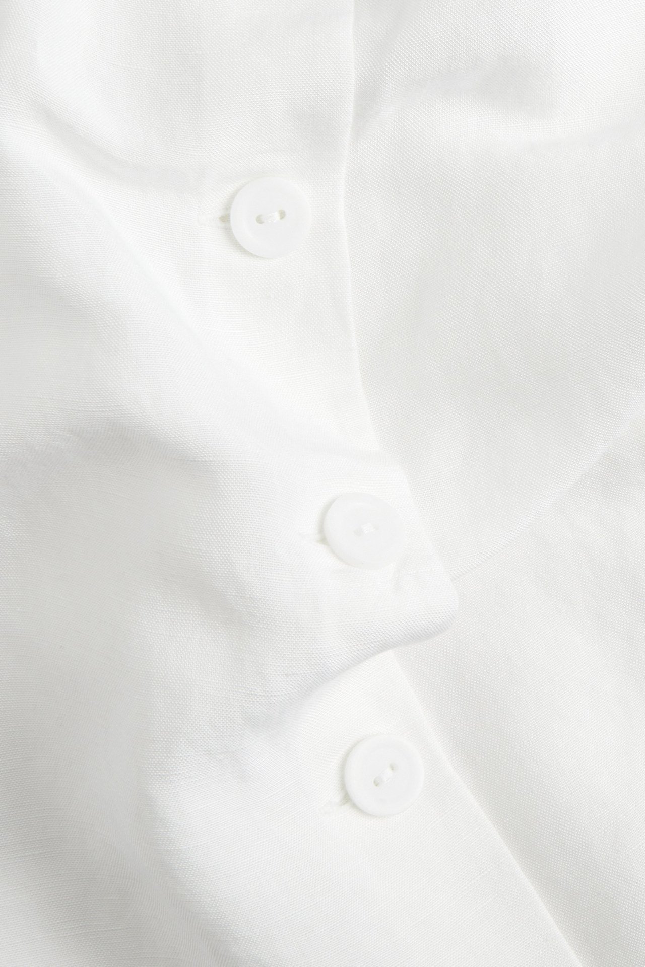 Zbliżenie białego topu z mieszanki lnu z trzema białymi guzikami.