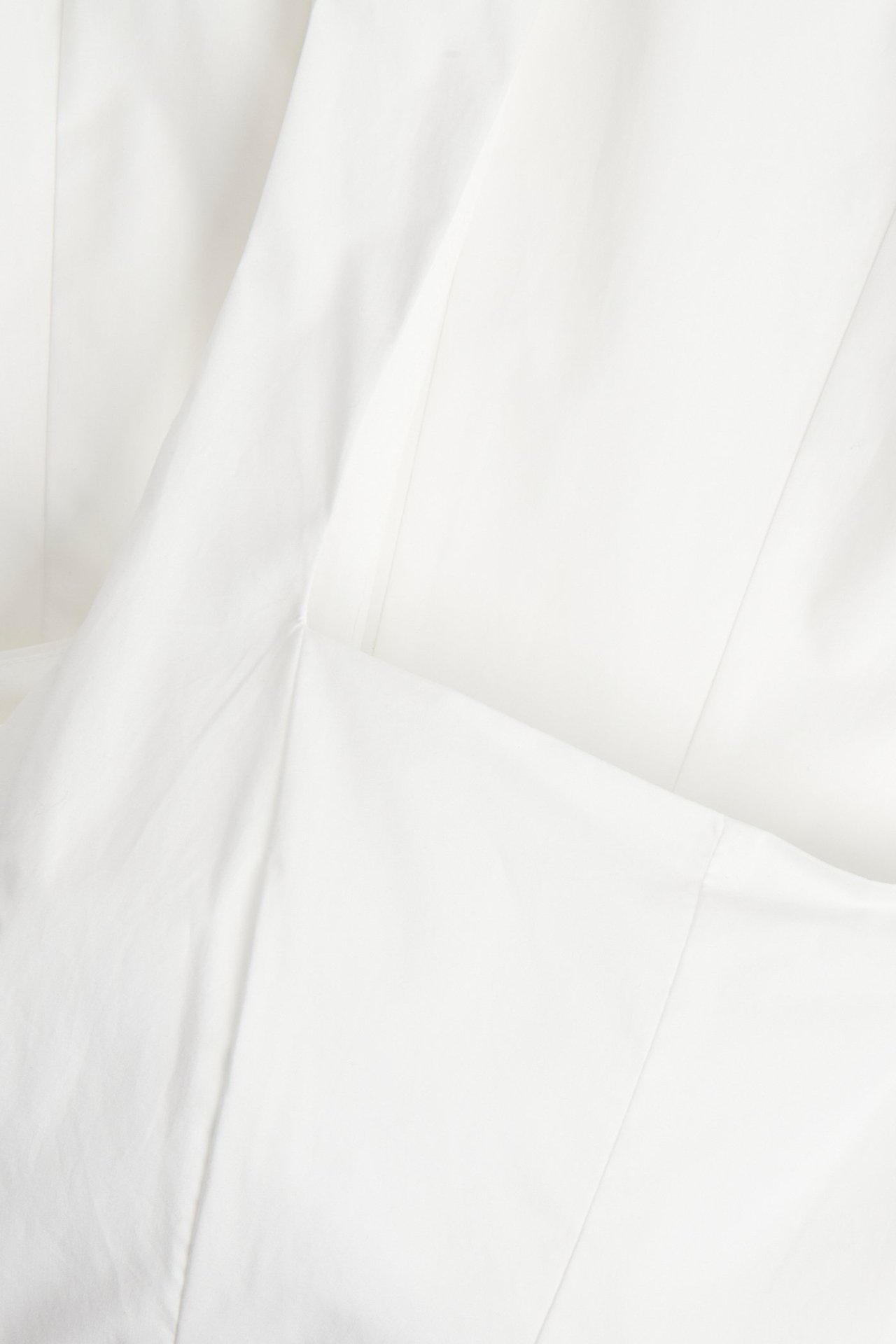Zbliżenie białej tkaniny popelinowej sukienki, ukazujące fałdy i szwy.