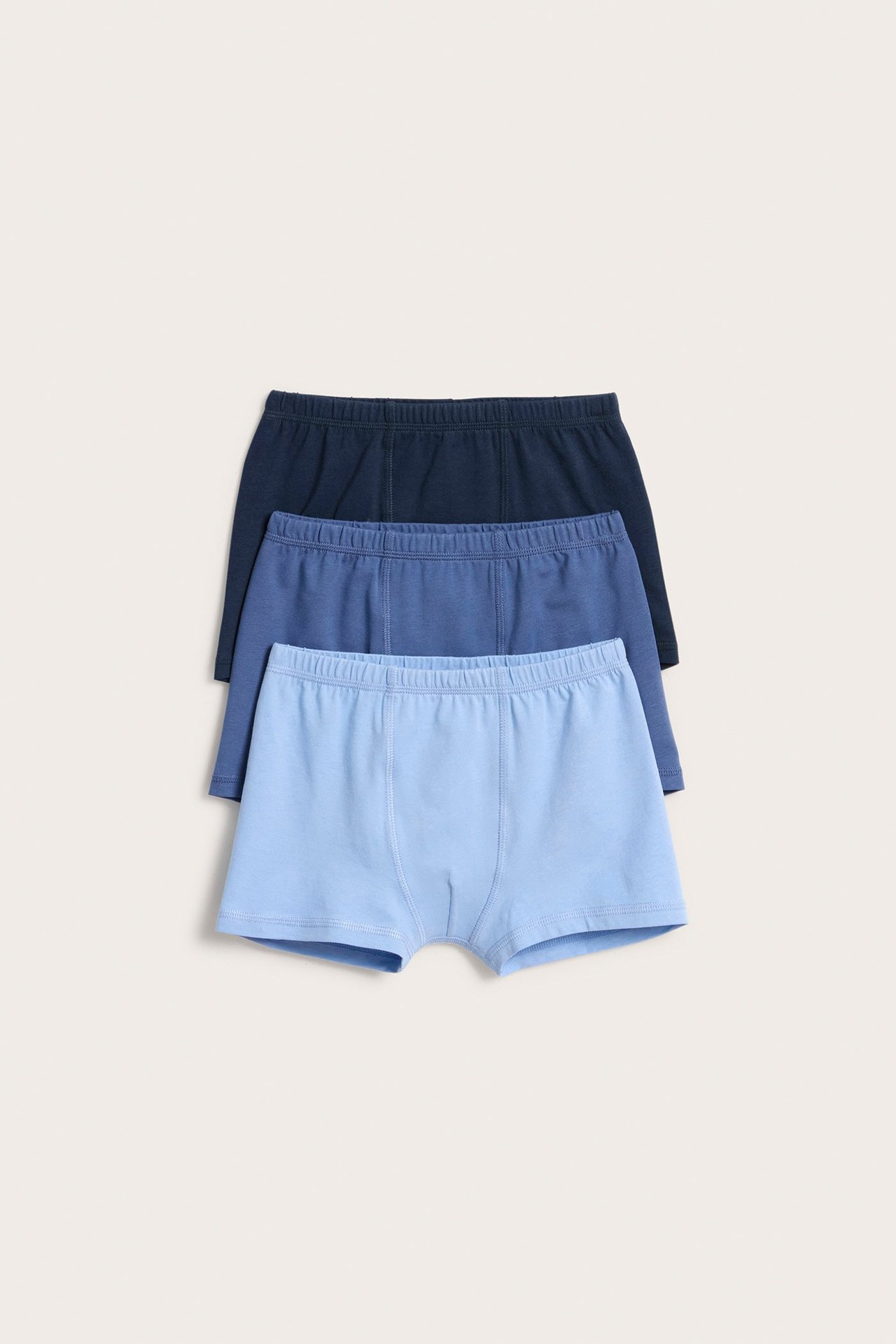 Edestä näkymä kolmesta yksivärisestä lasten puuvillabokserista: vaaleansininen, keskisininen ja tummansininen.