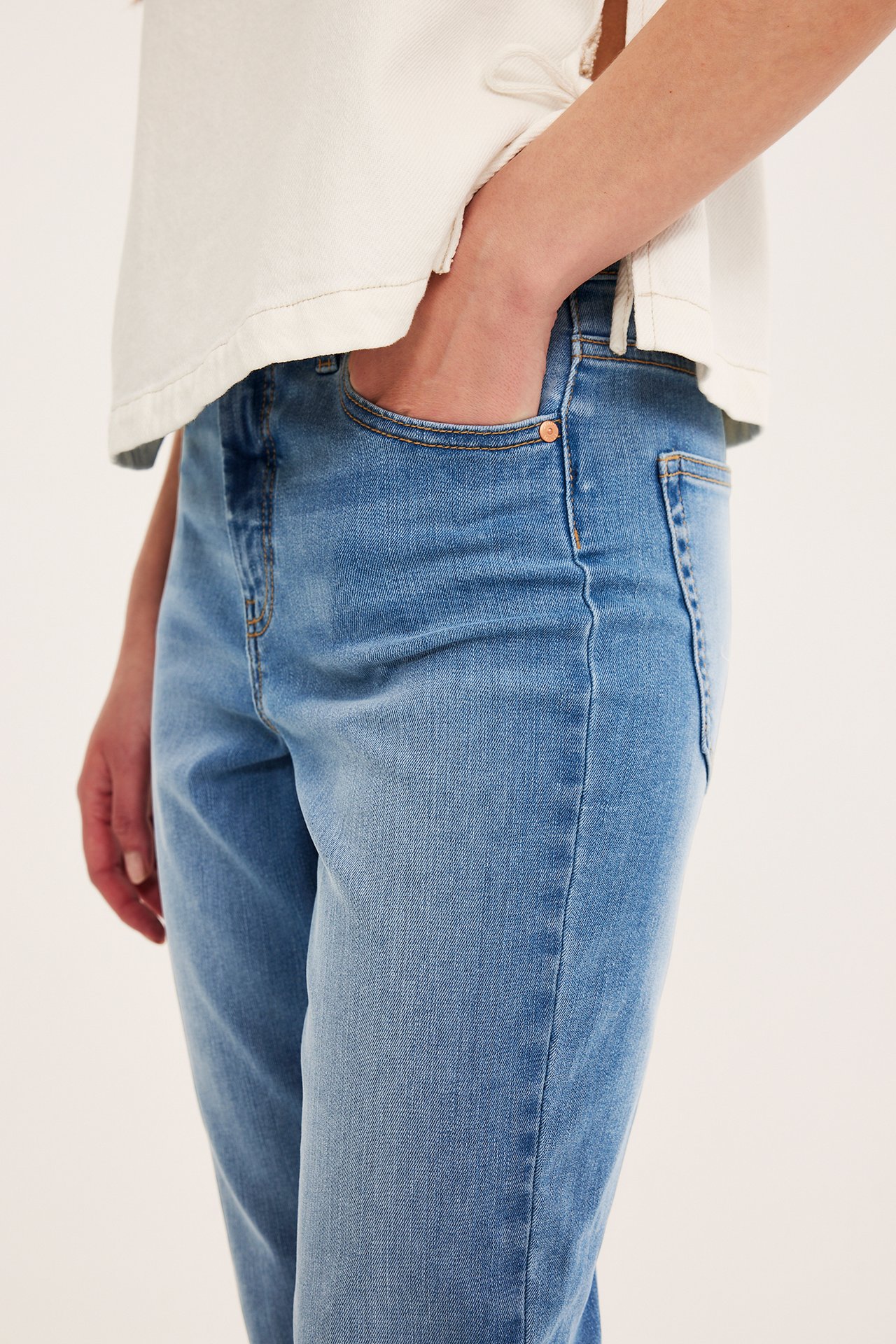 Närbild på kvinna i ljusblå croppade high-waist 5-ficks stretchjeans och en vit topp.