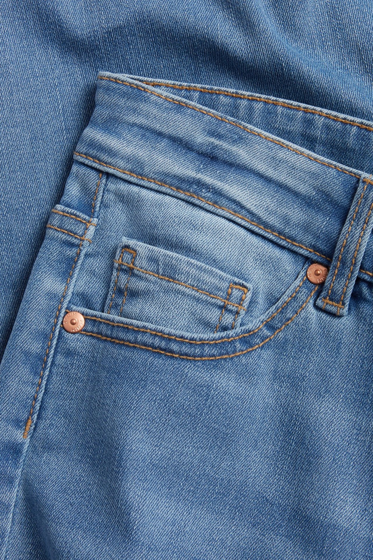 Zbliżenie na jasnoniebieskie dżinsy capri z wysokim stanem, z kieszeniami, miedzianymi nitami i kontrastowymi szwami.