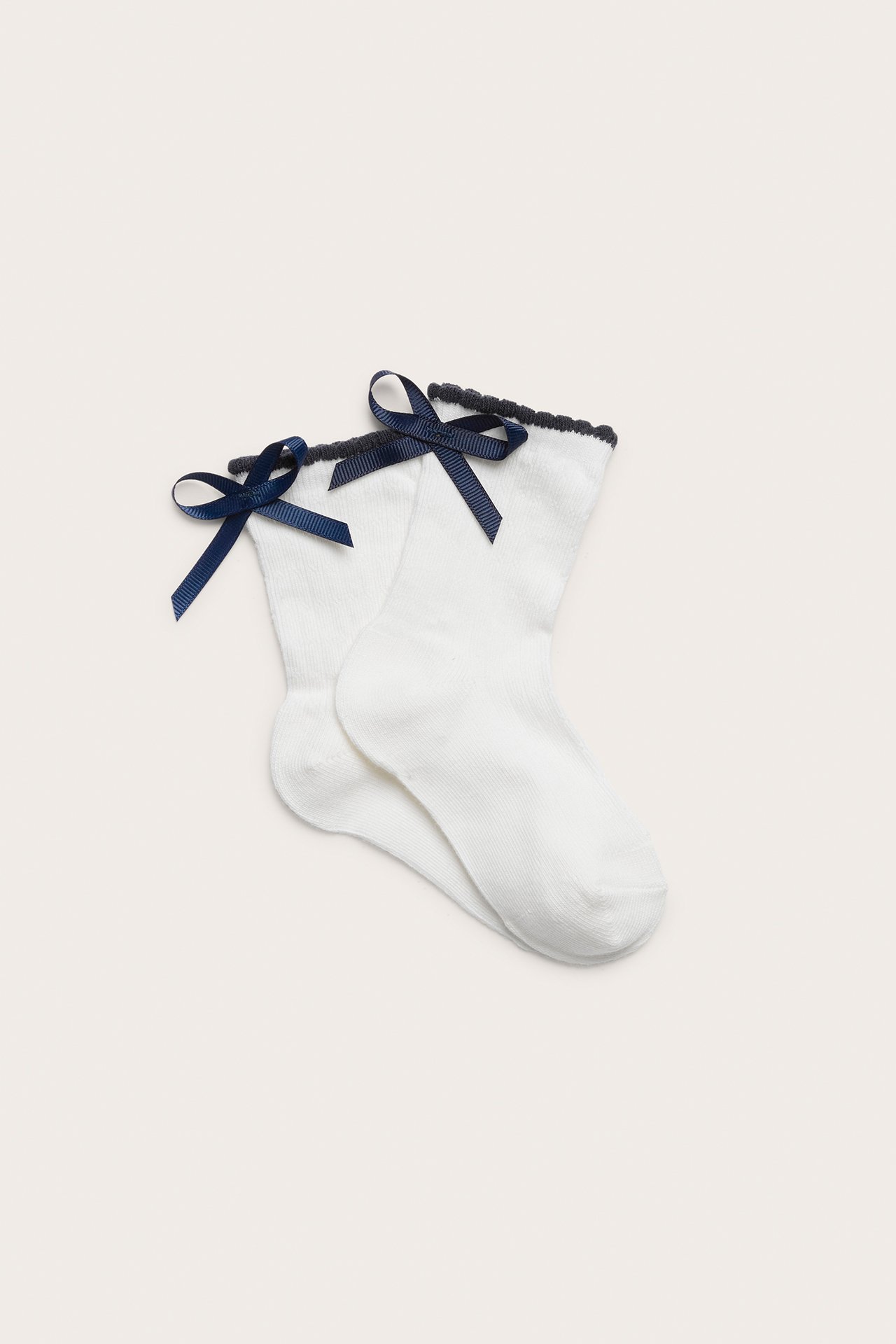Uppifrån sett par offwhite strumpor med mörkblå rosetter och mörk uddkant.