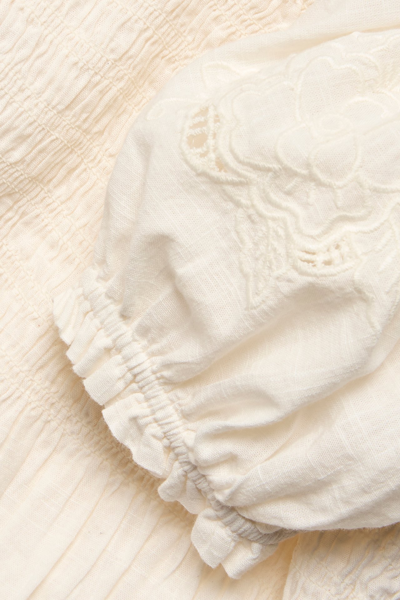 Närbild av en offwhite bomullsblus med smockdetaljer, broderad puffärm och resår i ärmslut.