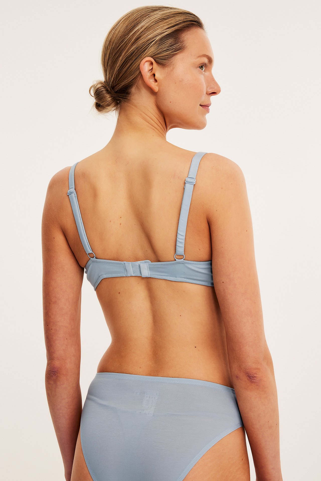 Naisen selkäkuva yllään vaaleansininen lyocell-bralette säädettävillä olkaimilla ja yhteensopivat alushousut.