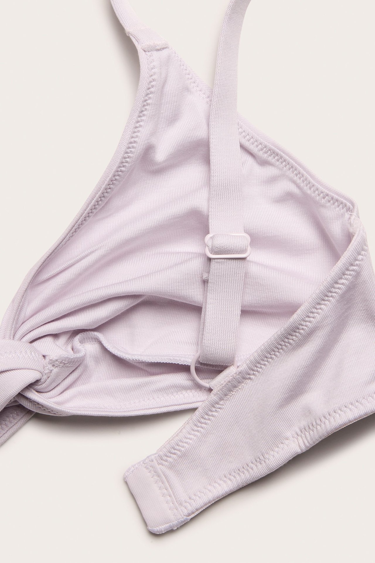 Zbliżenie na jasnoróżowy lyocellowy biustonosz bralette z węzłem z przodu i regulowanym ramiączkiem.