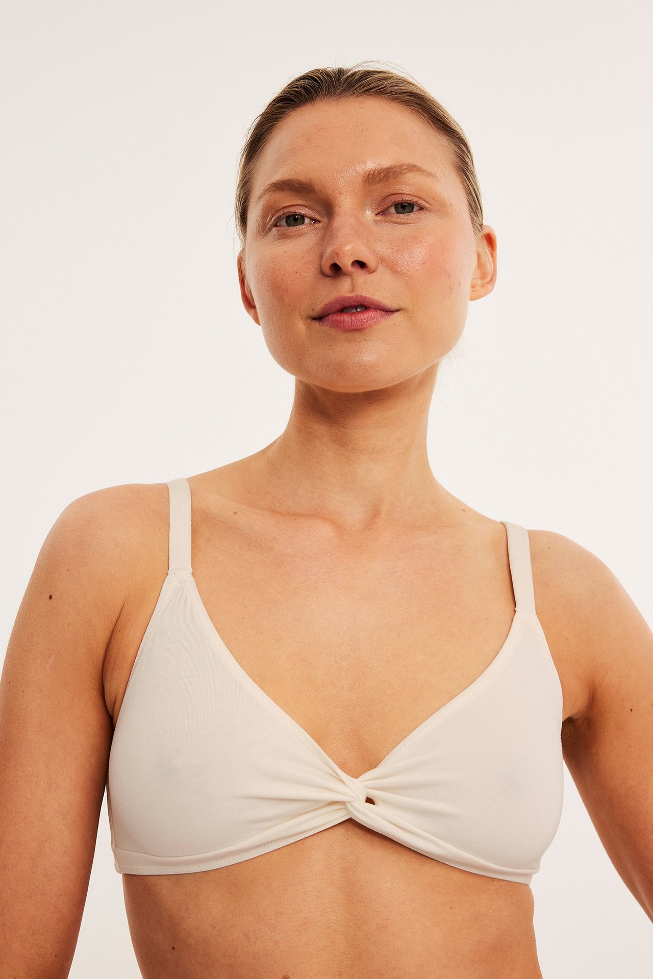 Framifrån, kvinna i vit lyocell bralette med knutdetalj framtill och justerbara axelband.