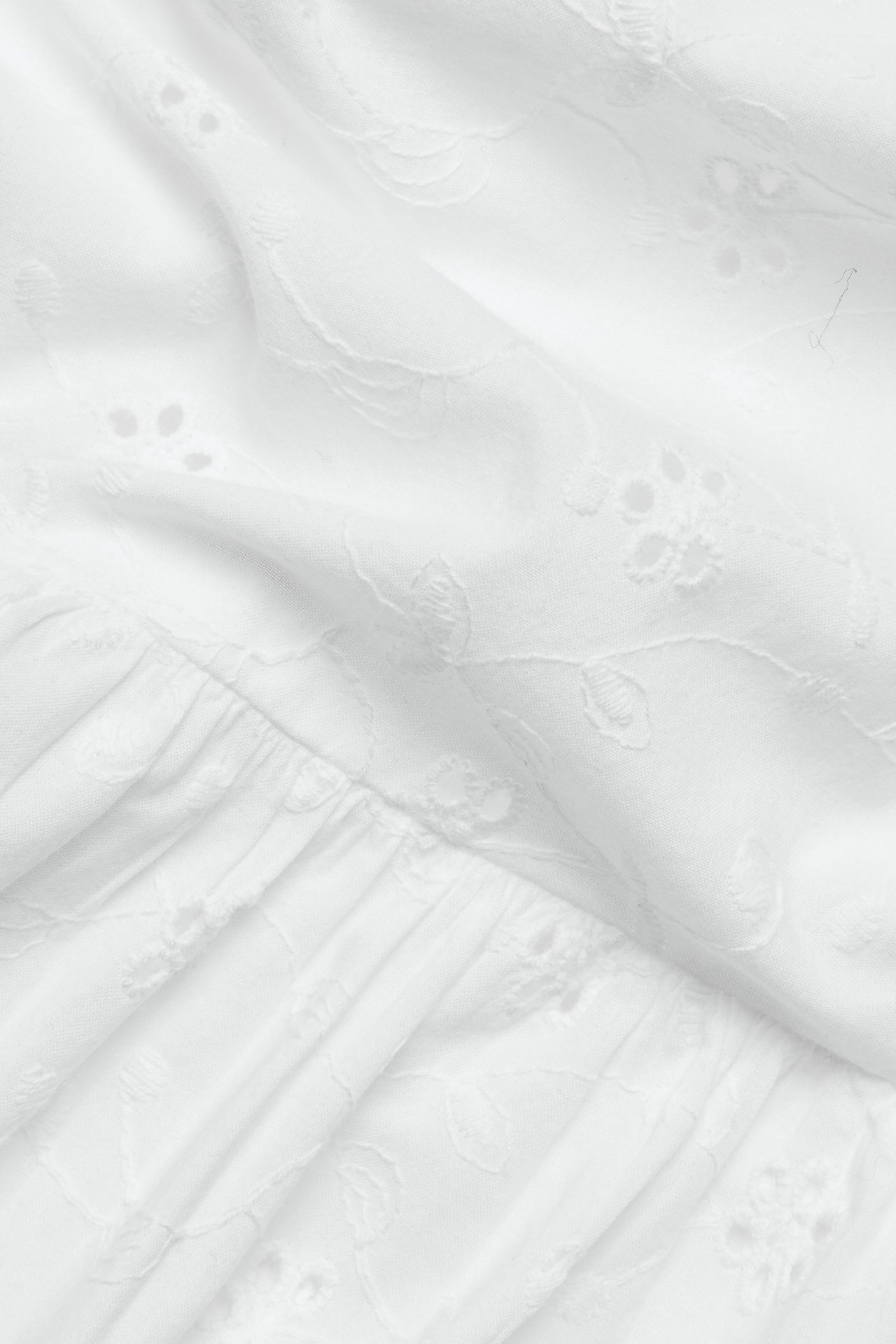 Zbliżenie białej bawełnianej bluzki peplum z haftem angielskim i falbanką.