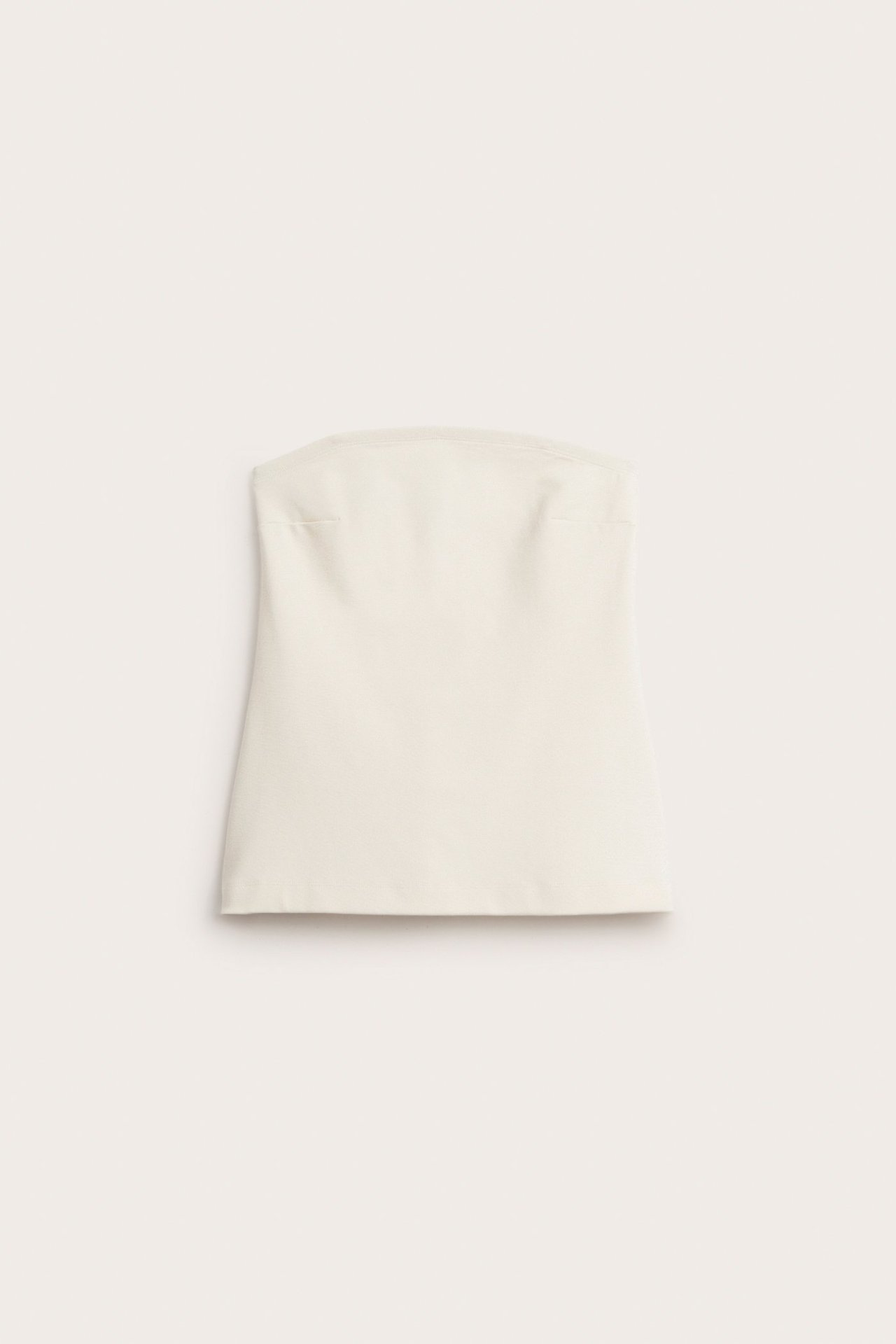 Widok z przodu: dłuższy, kremowy top bez ramiączek z jednolitego elastycznego materiału, ułożony płasko.