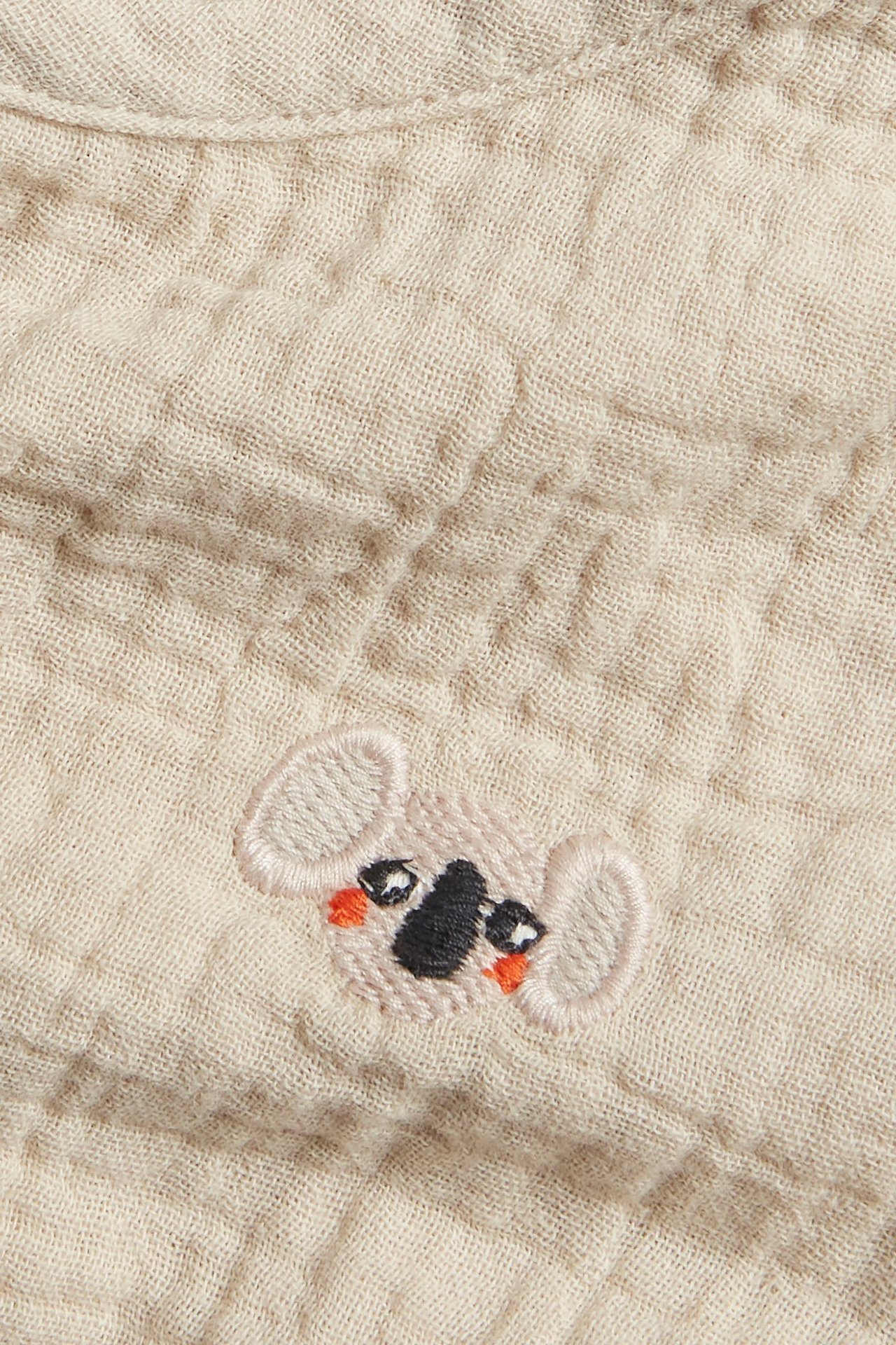 Zbliżenie na jasnobeżowy muślinowy top dla niemowląt z haftowaną twarzą koali.