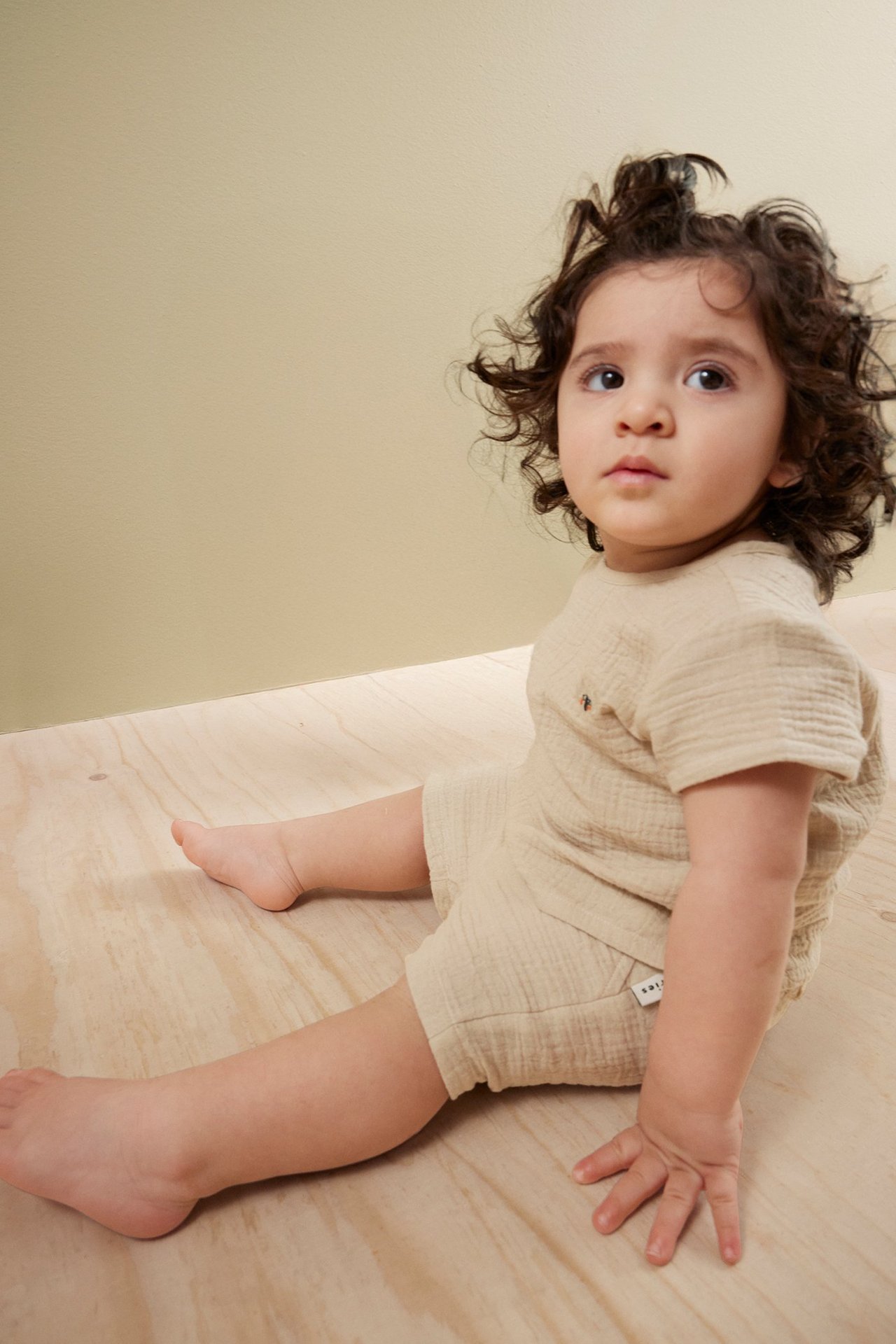 Widok z przodu: niemowlę w jasnobeżowym, krótkim topie muślinowym i pasujących szortach.