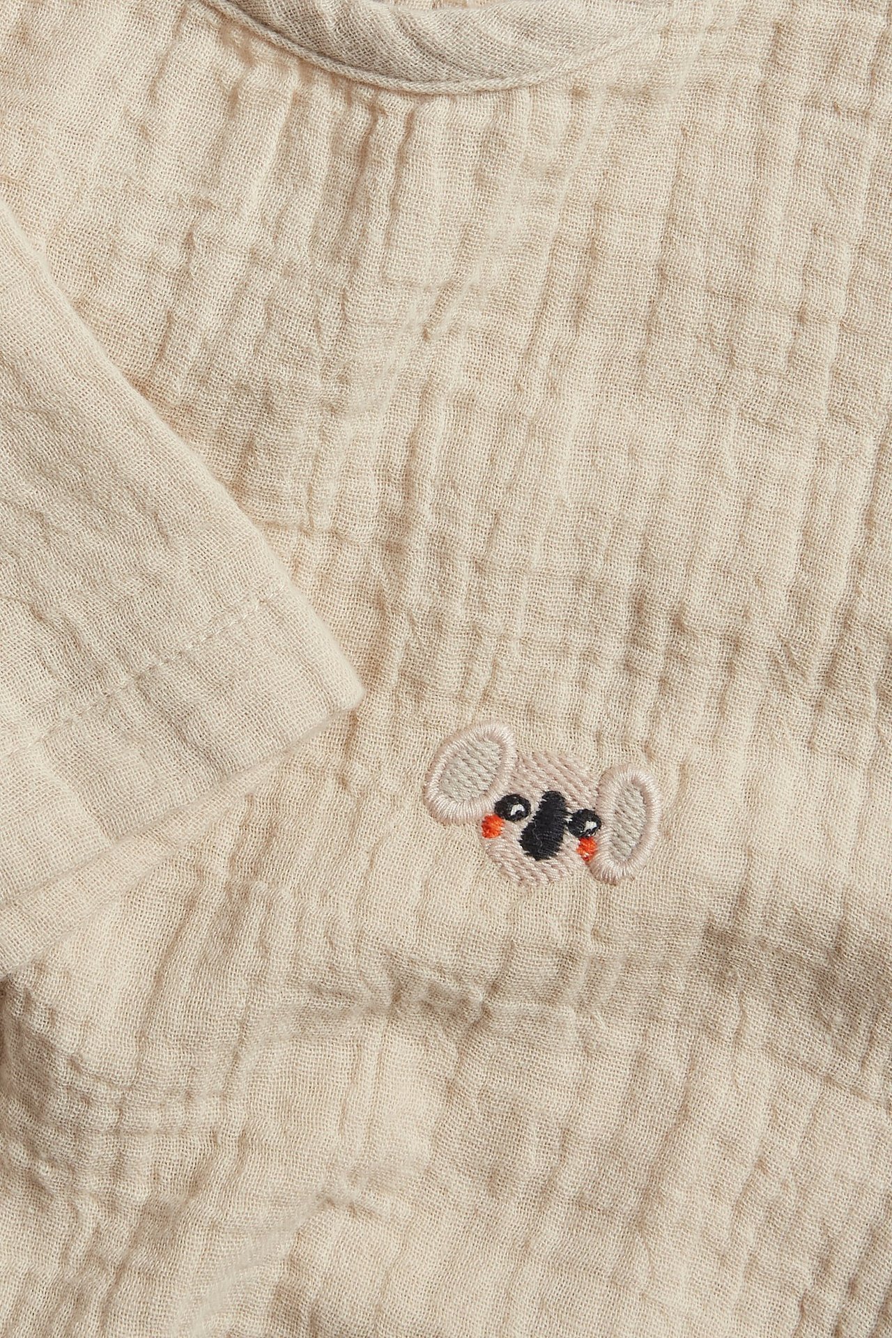 Zbliżenie na beżowy, muślinowy, krótki top dziecięcy z haftem koali.