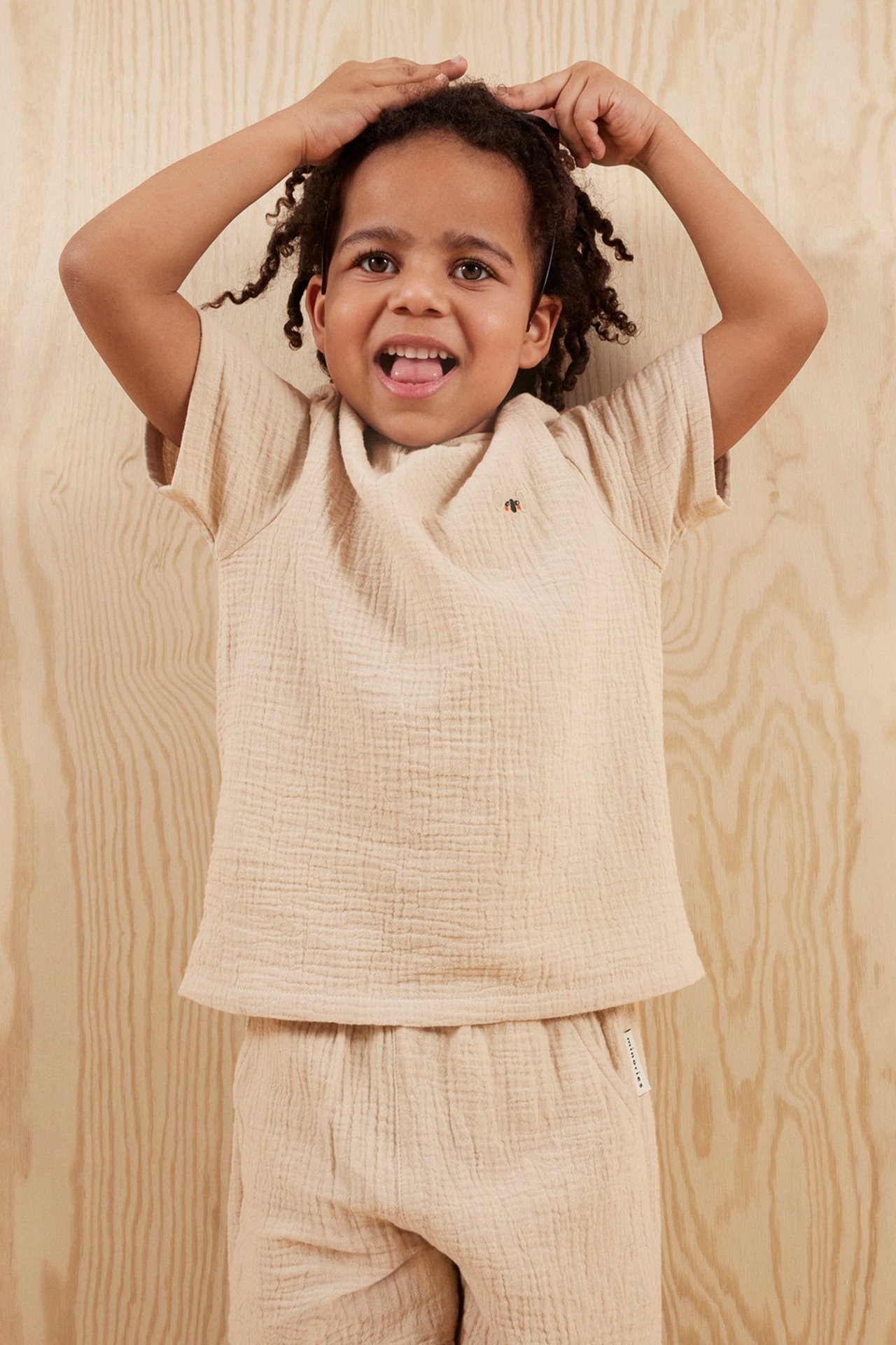 Widok z przodu dziecka w jasnobeżowym, krótkim topie muślinowym i pasujących szortach.