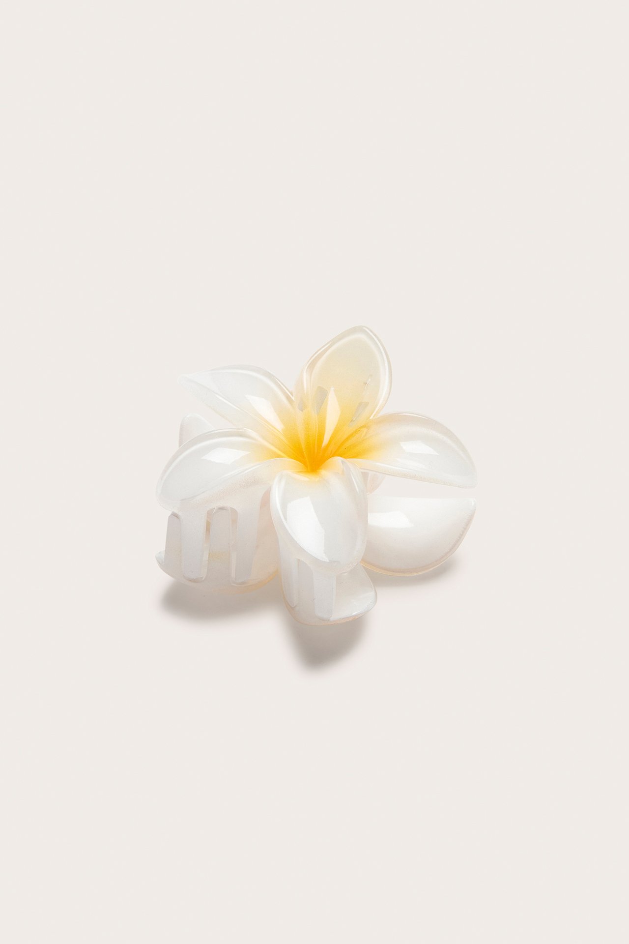 Lähikuva valkoisesta muovisesta kukkamuotoisesta hiusklipsistä, jossa keltainen keskusta.