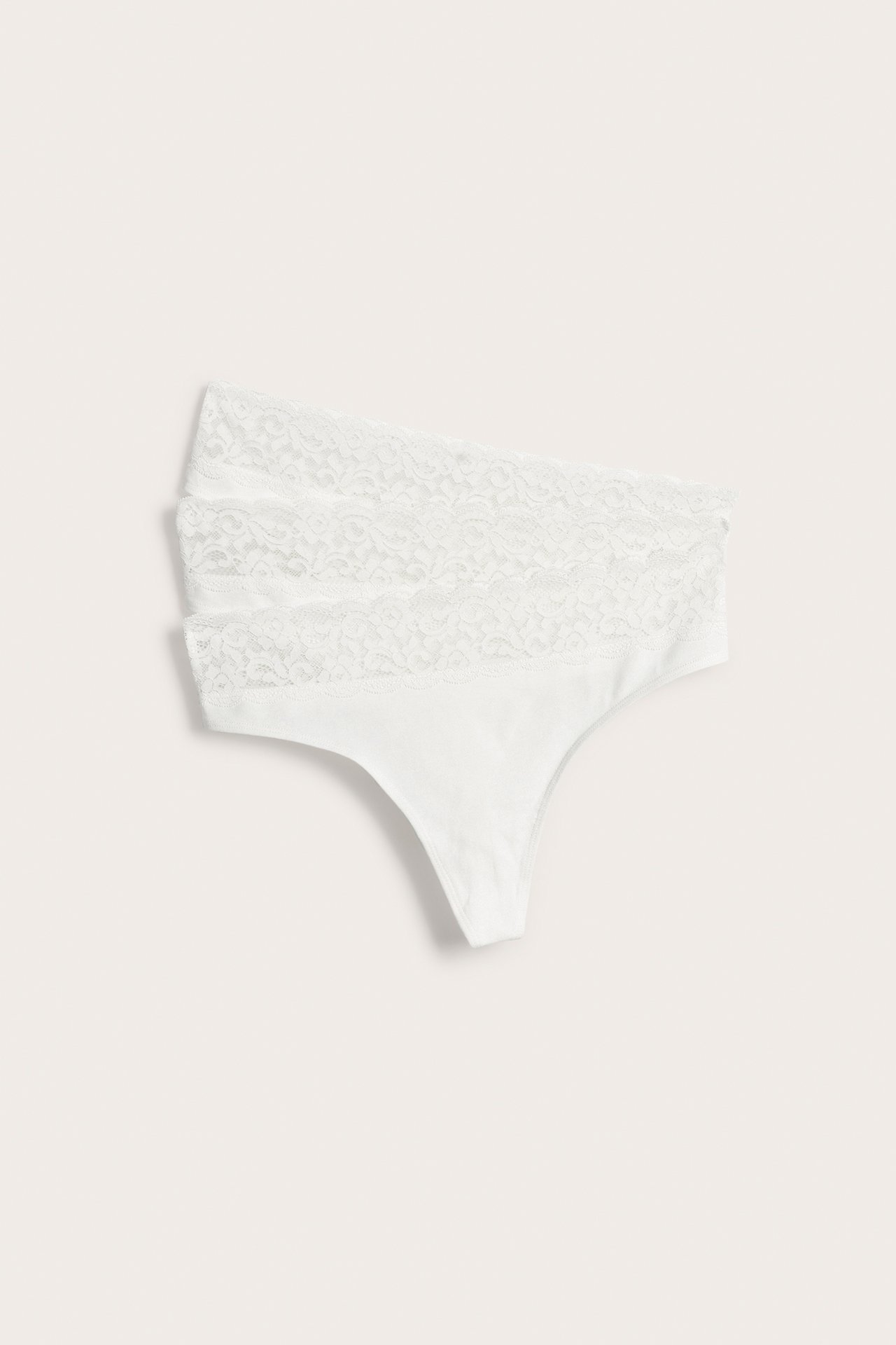 Frontvisning av tre stablede hvite bomullsblandingsstringtruser med bred blondekant i midjen.