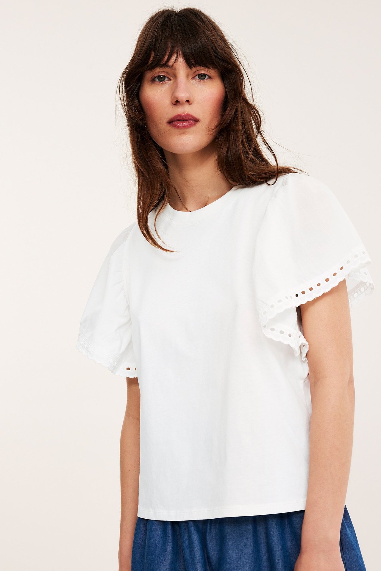 Framifrån: kvinna i offwhite bomullstopp med korta volangärmar och broderade hålmönster.