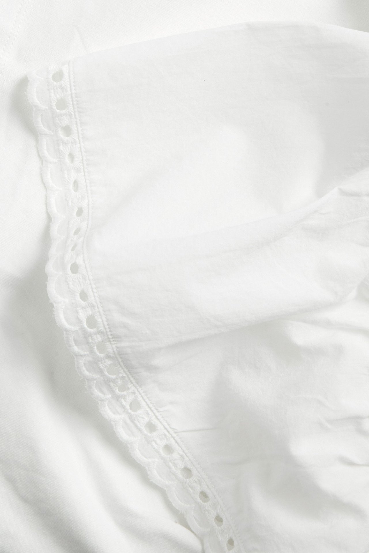 Zbliżenie na ecru bawełniany top z falbanką i haftowanym brzegiem.