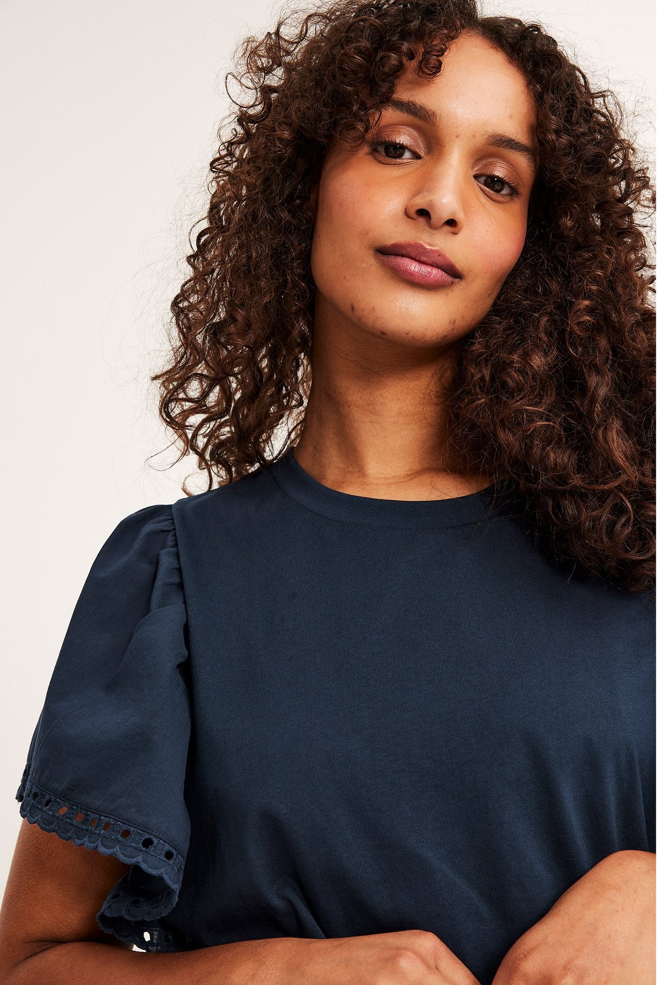 Närbild framifrån på en kvinna i mörkblå bomullstopp med puffärmar och broderad kant.