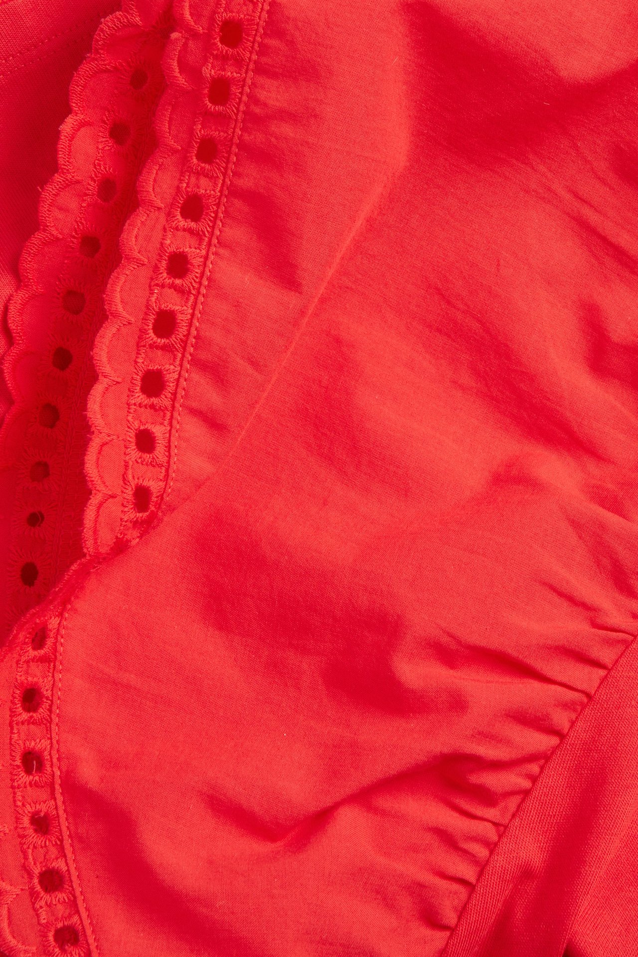 Zbliżenie czerwonego bawełnianego topu z falbanami i haftem angielskim.