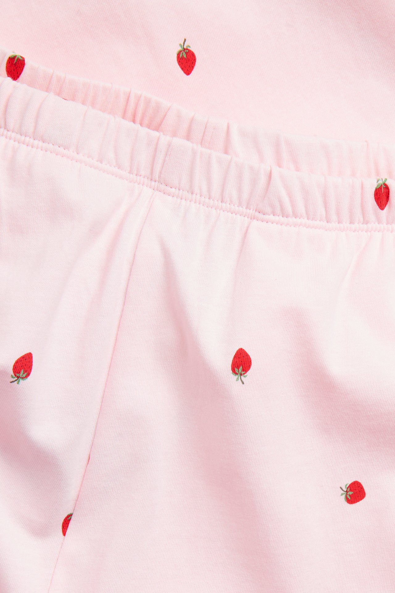 Nærbilde av rosa pyjamasbukser i bomull med rødt jordbærmønster og elastisk midje.