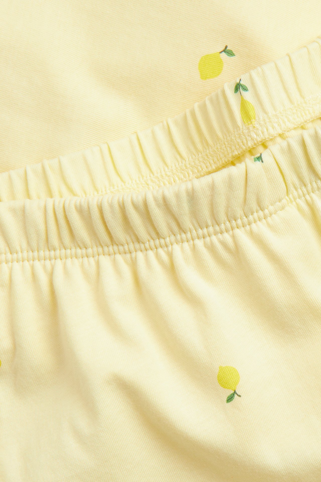 Närbild av ljusgula pyjamasbyxor i bomullstrikå med små citronmönster och resår i midjan.