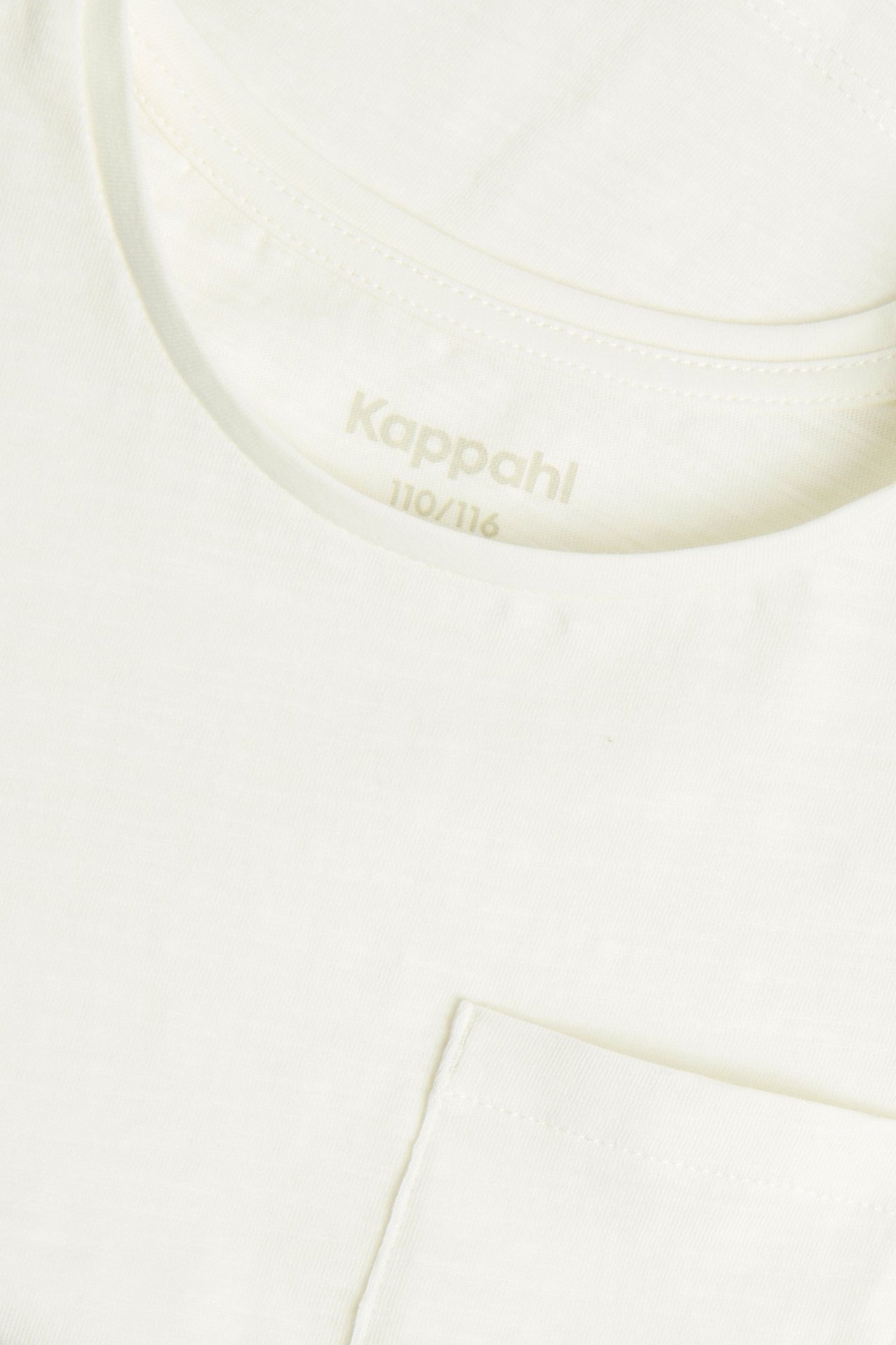 Zbliżenie na dziecięcy top z bawełny w kolorze ecru, z fakturą i kieszonką na piersi.