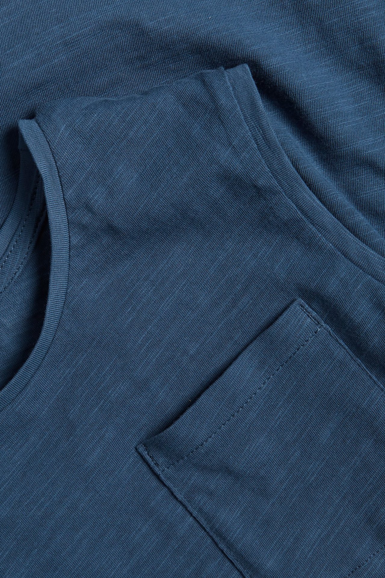 Zbliżenie na ciemnoniebieski bawełniany top z teksturą i kieszenią na piersi.