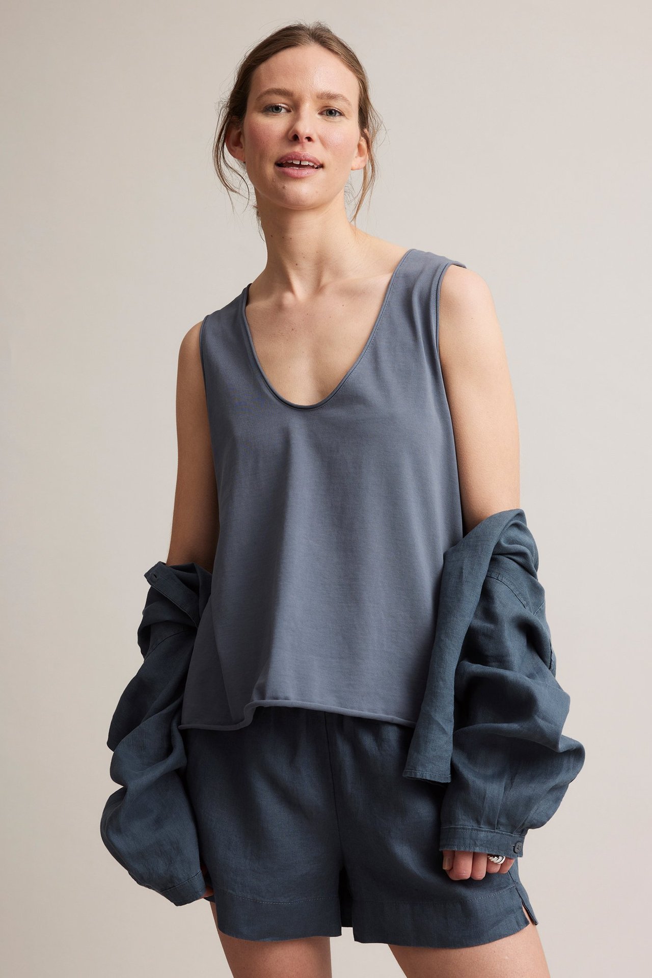 Frontutsikt: Kvinne i mørkeblå V-hals bomullstopp, mørkeblå shorts og en mørkeblå skjorte drapert.