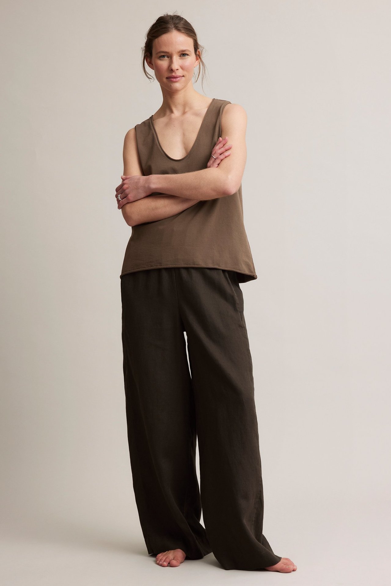 Forfra: kvinne i brun V-hals bomullstopp med rå kant og mørke vide bukser.