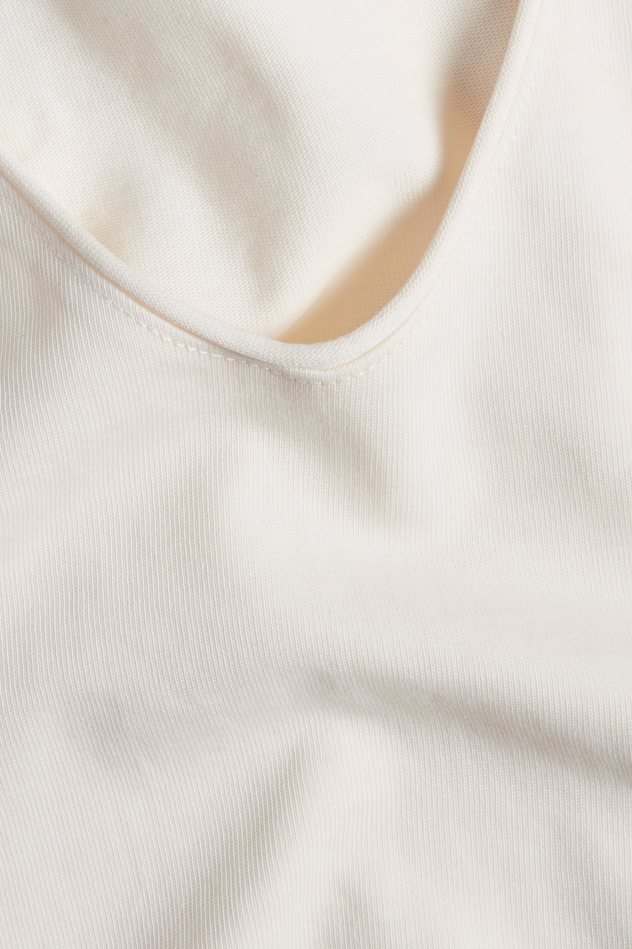 Närbild av ett off-white V-ringat linne i bomullstrikå med en subtil ribbad struktur.