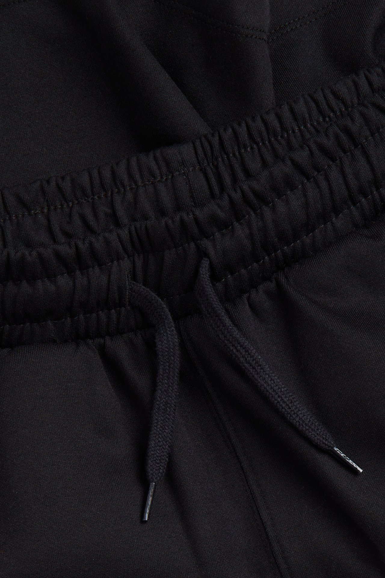 Närbild av svarta interlock-shorts med elastisk midja och svart dragsko med plaständar.