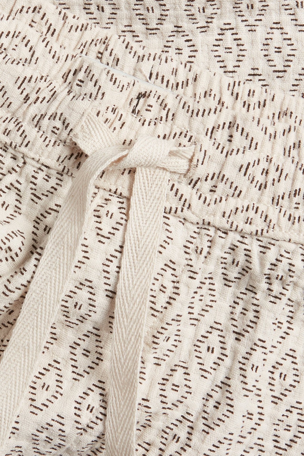 Zbliżenie na jasnobeżowe męskie szorty bawełniane z ciemnym geometrycznym wzorem i zawiązanym sznurkiem.