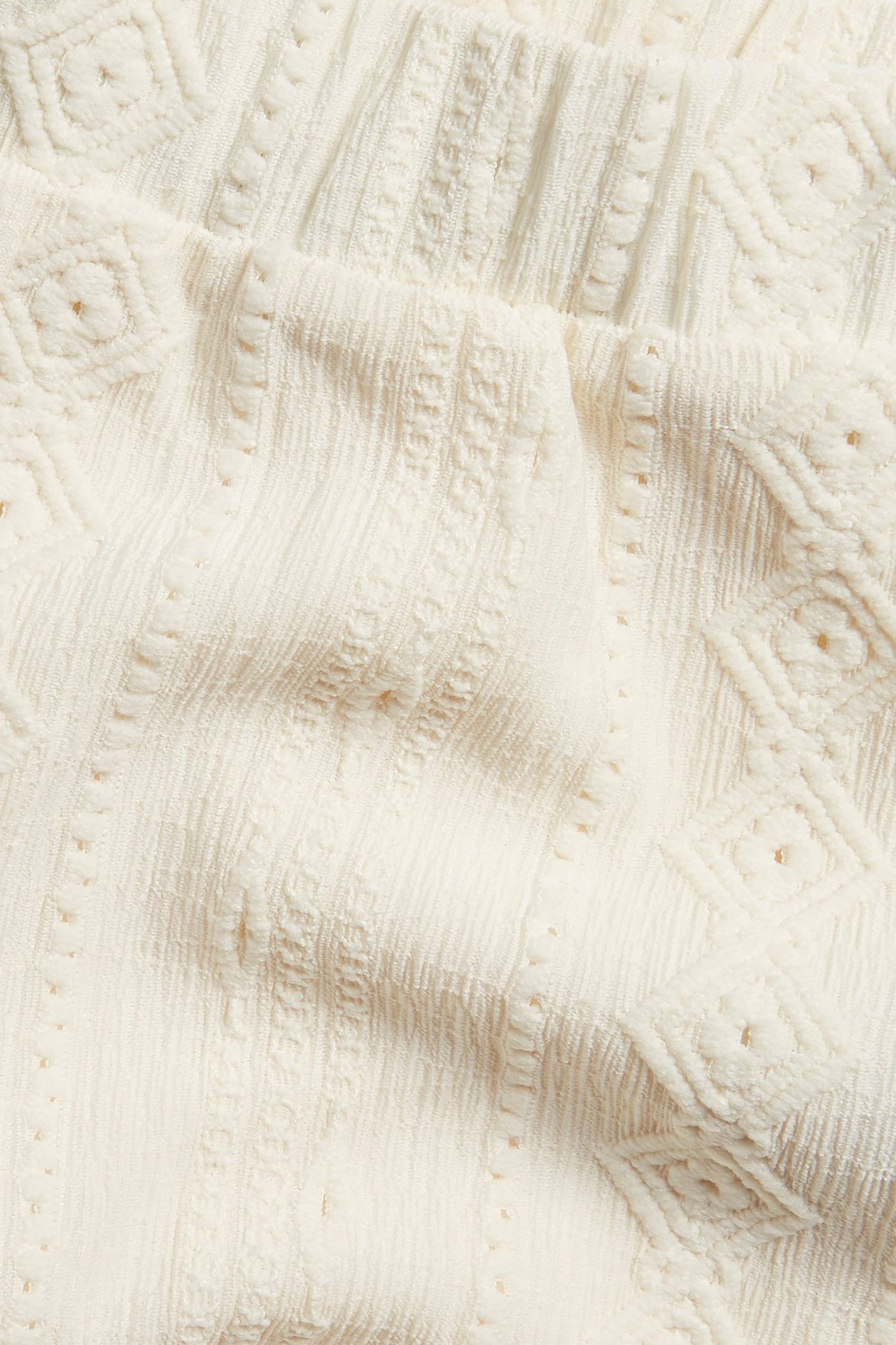 Zbliżenie na ecru szorty dżersejowe z teksturowanym wzorem przypominającym koronkę i elastyczną talią.