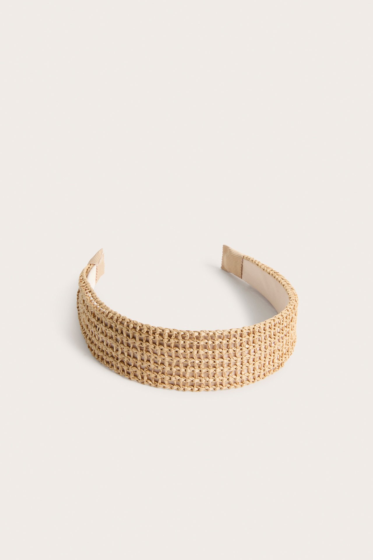 Frontvy av ett brett, ljusbeige flätat diadem med stråliknande textur.