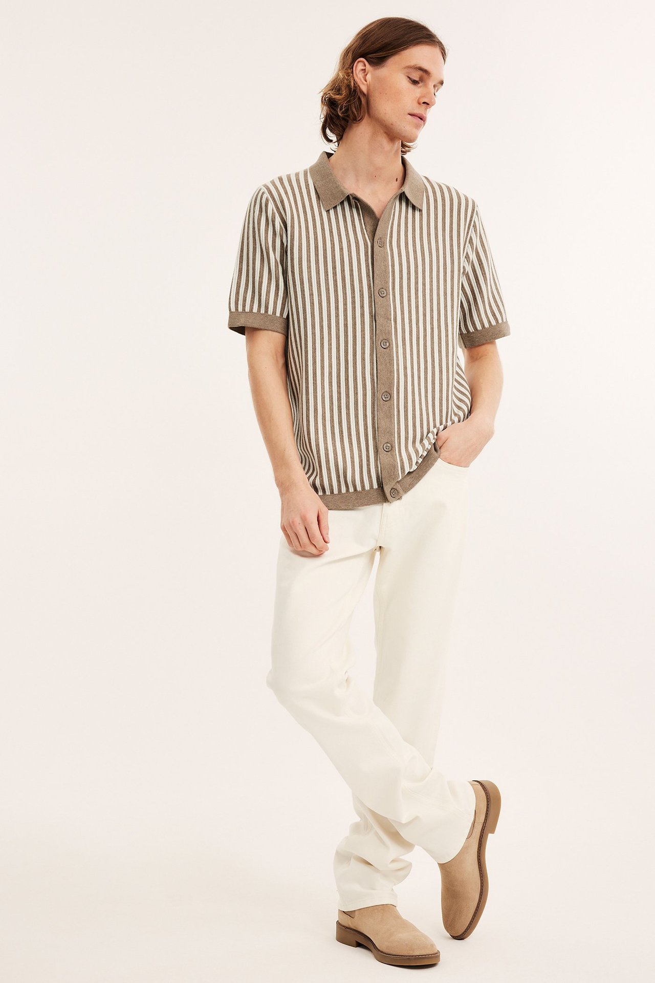 Edestä: mies beigemelange raidallisessa neulepikeepaidassa, kermanvärisissä housuissa ja beigissä mokkakengissä.