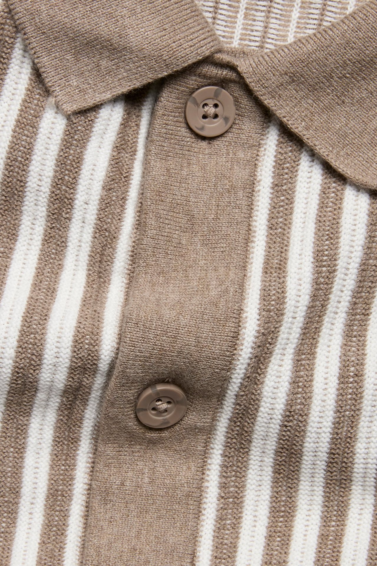 Zbliżenie beżowo-białej, prążkowanej, dzianinowej koszulki polo z bawełny, z zapięciem na guziki.