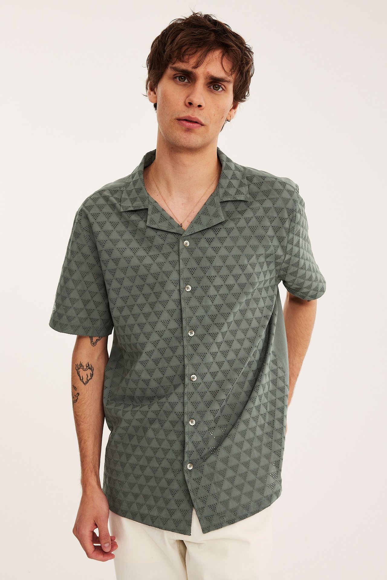 Edestä, mies vihreässä lyhythihaisessa puuvillapaidassa, jossa rei'itetty kolmiokuvio, ja vaaleat housut.