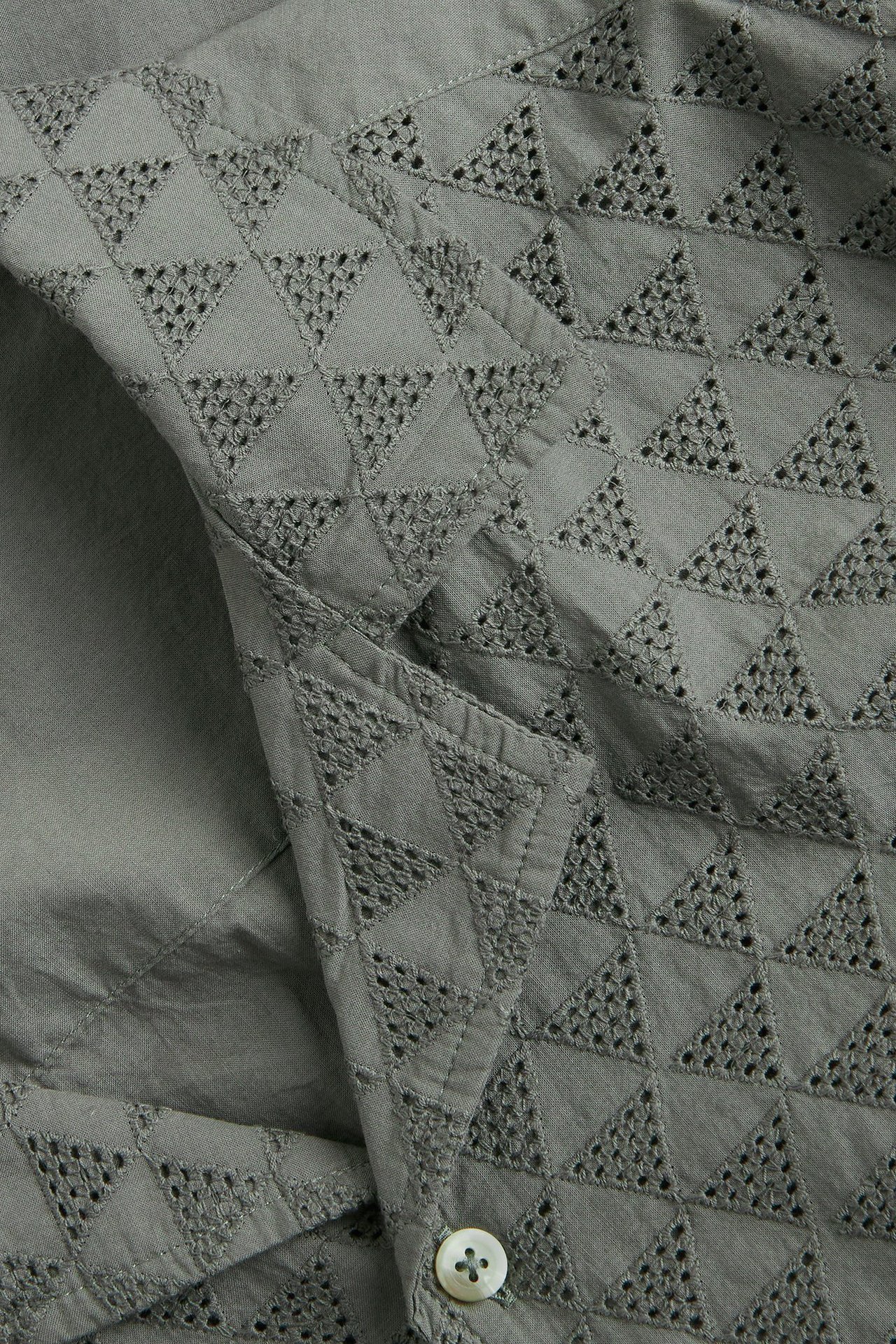 Zbliżenie zielonej męskiej koszuli z krótkim rękawem z bawełny, z trójkątnym haftem angielskim i białym guzikiem.