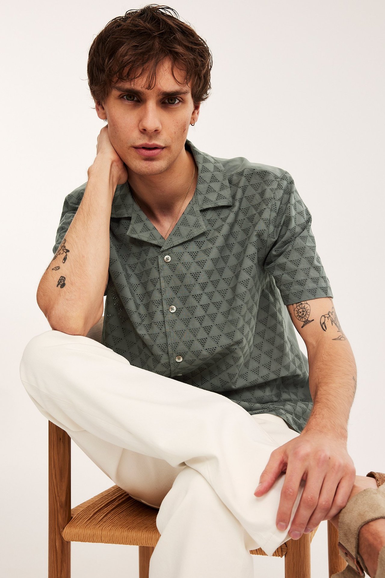 Edestä, mies vihreässä lyhythihaisessa paidassa, jossa kolmiomainen broderie anglaise, ja valkoisissa housuissa.