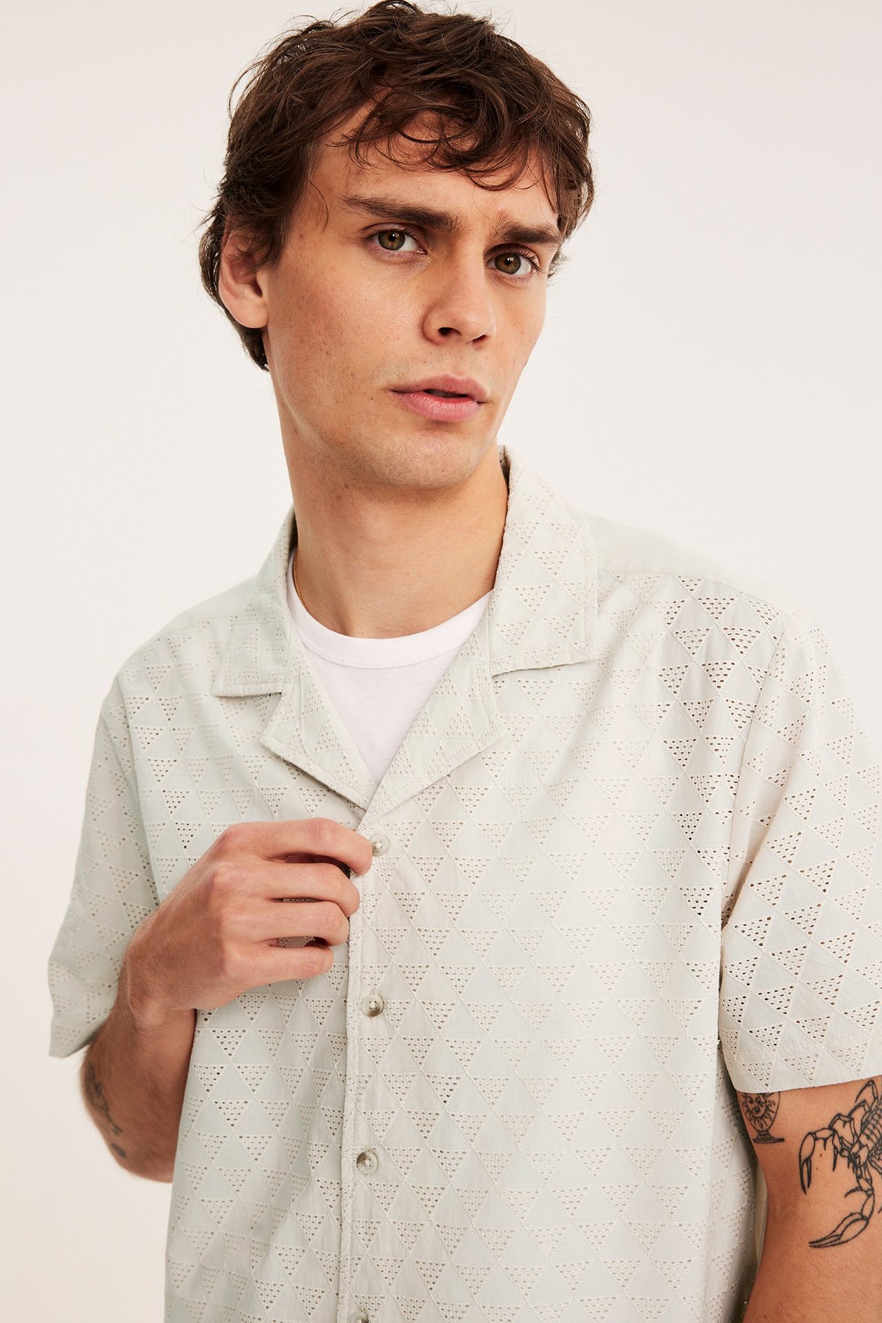 Mies edestä, vaaleanbeige lyhythihainen puuvillapaita broderie anglaise -kuviolla, valkoisen t-paidan päällä.