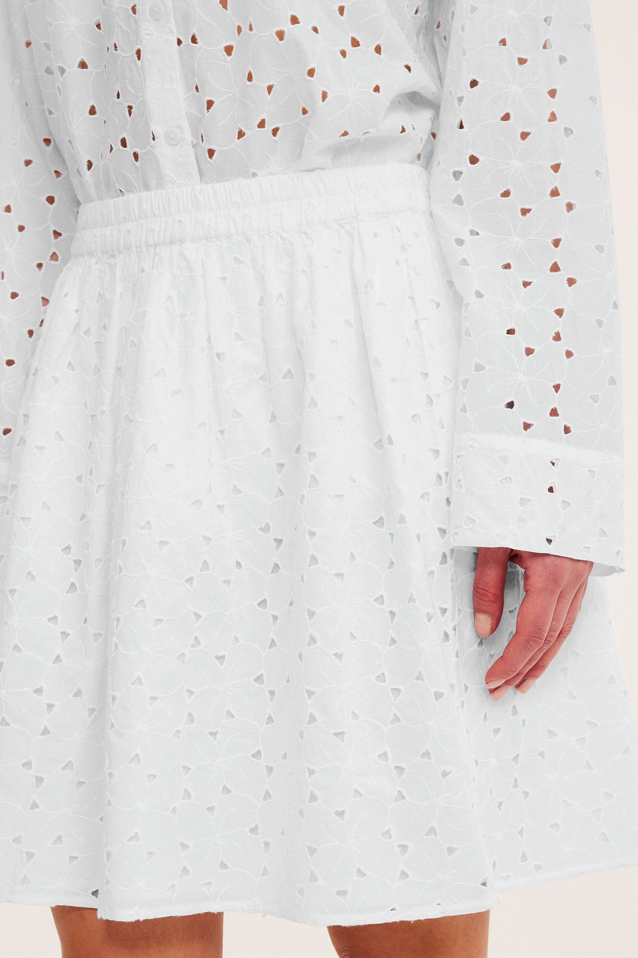 Kvinne i et hvitt kort brodert skjørt med elastisk midje og matchende hvit brodert skjorte.