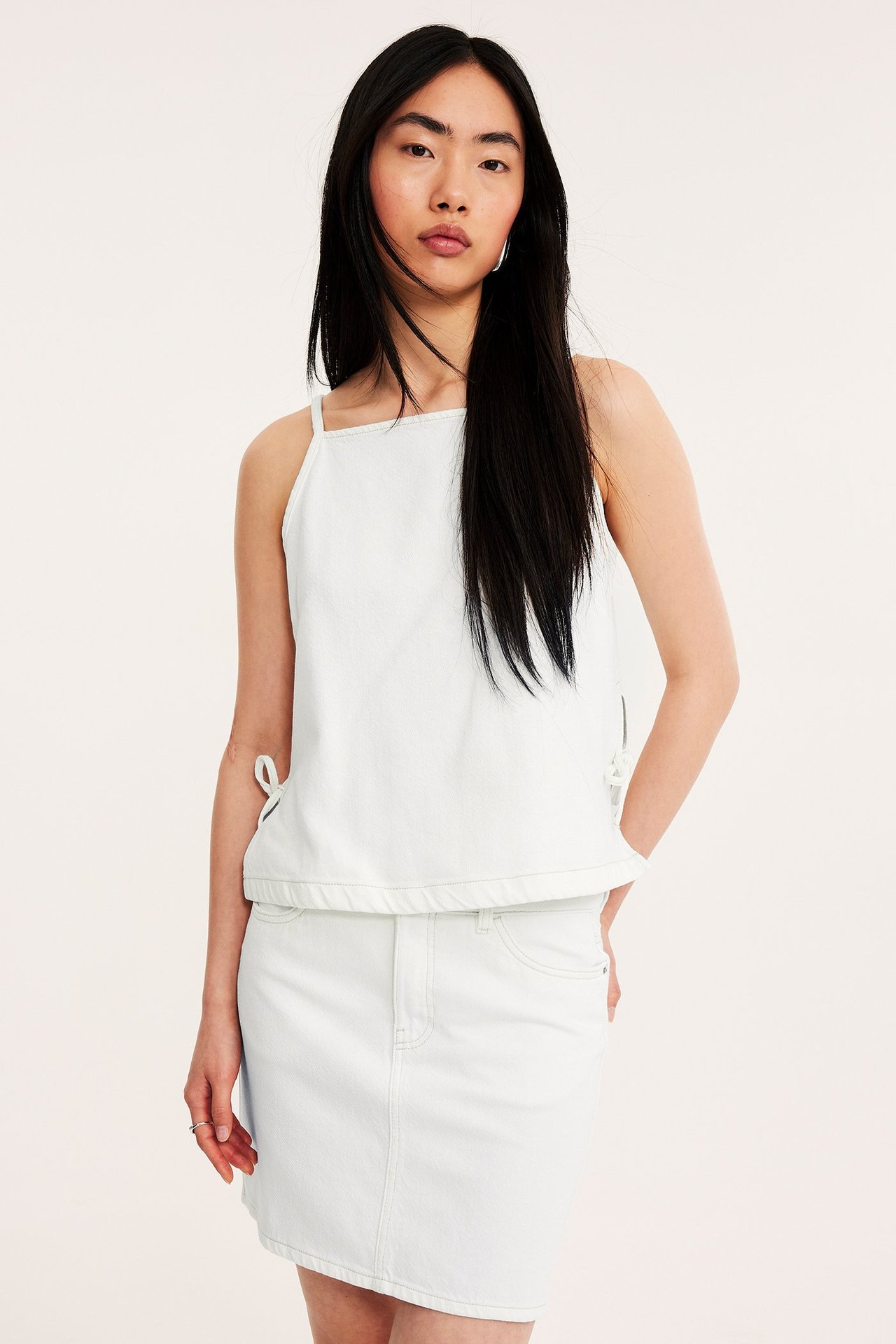 Frontbilde: kvinne i et hvitt kort twillskjørt og en hvit ermeløs topp med knyting.