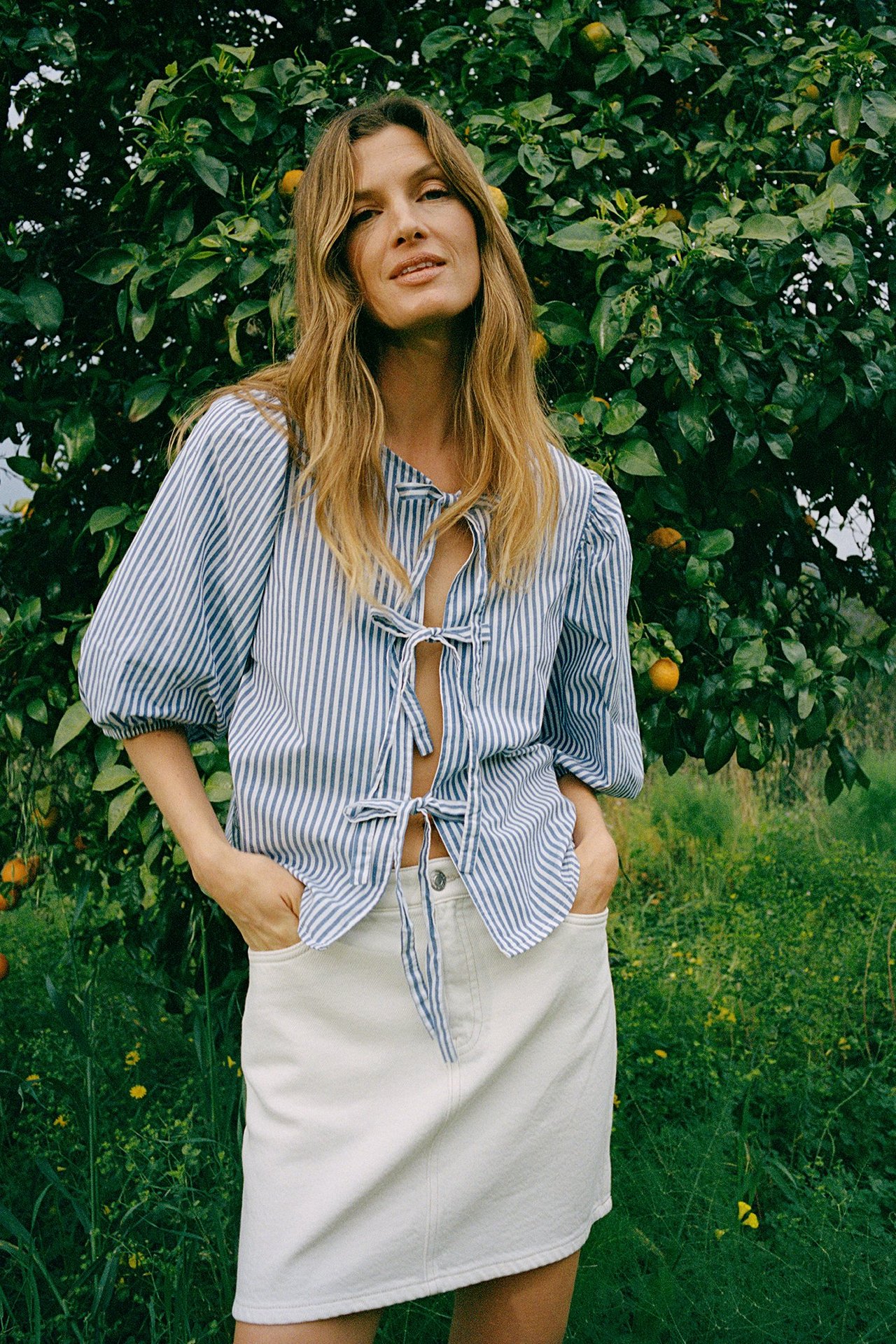 Forfra: kvinne i hvitt twill miniskjørt og blå- og hvitstripet bluse med knyting foran.