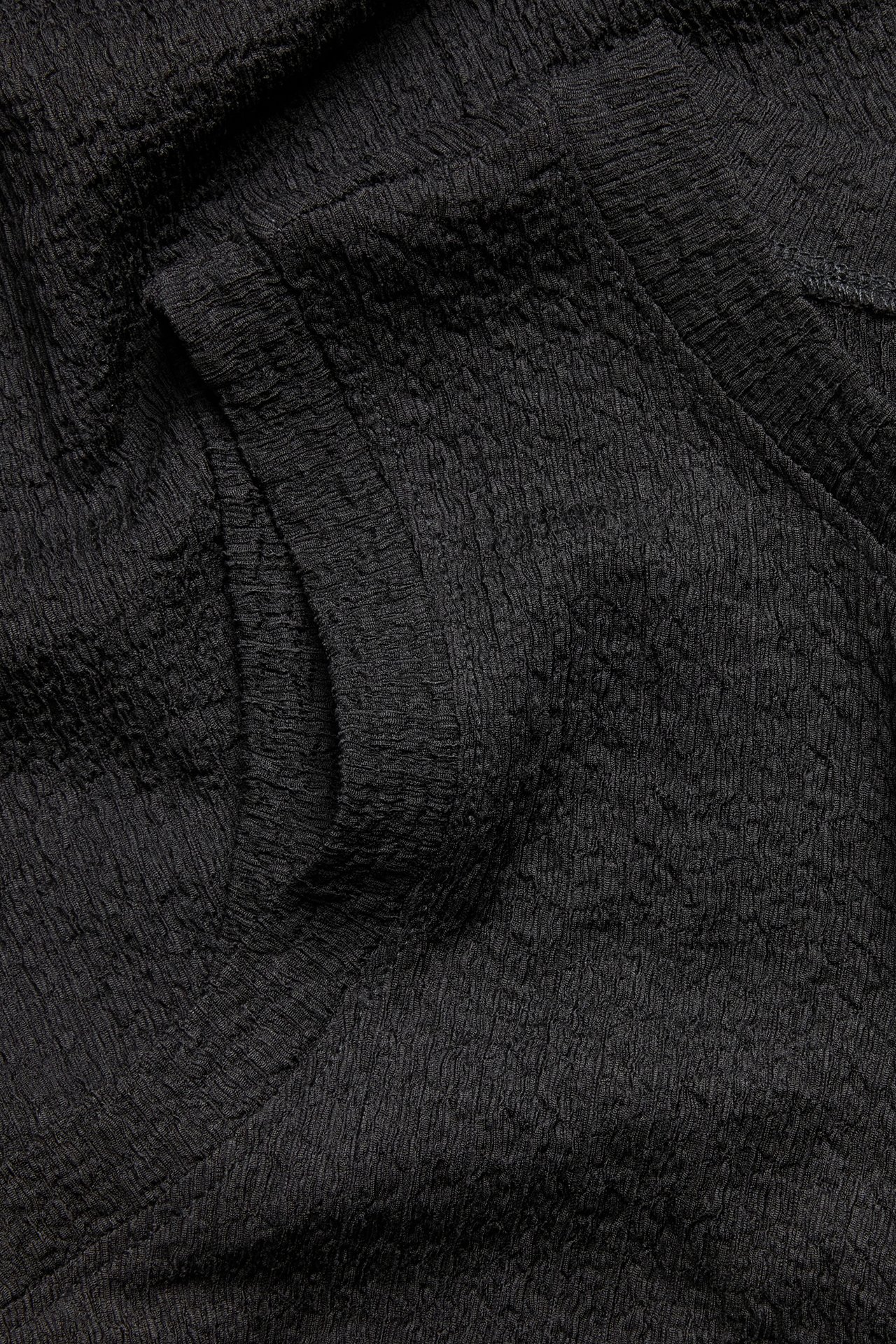 Närbild av svart strukturerat klänningstyg, som visar dess texturerade yta.