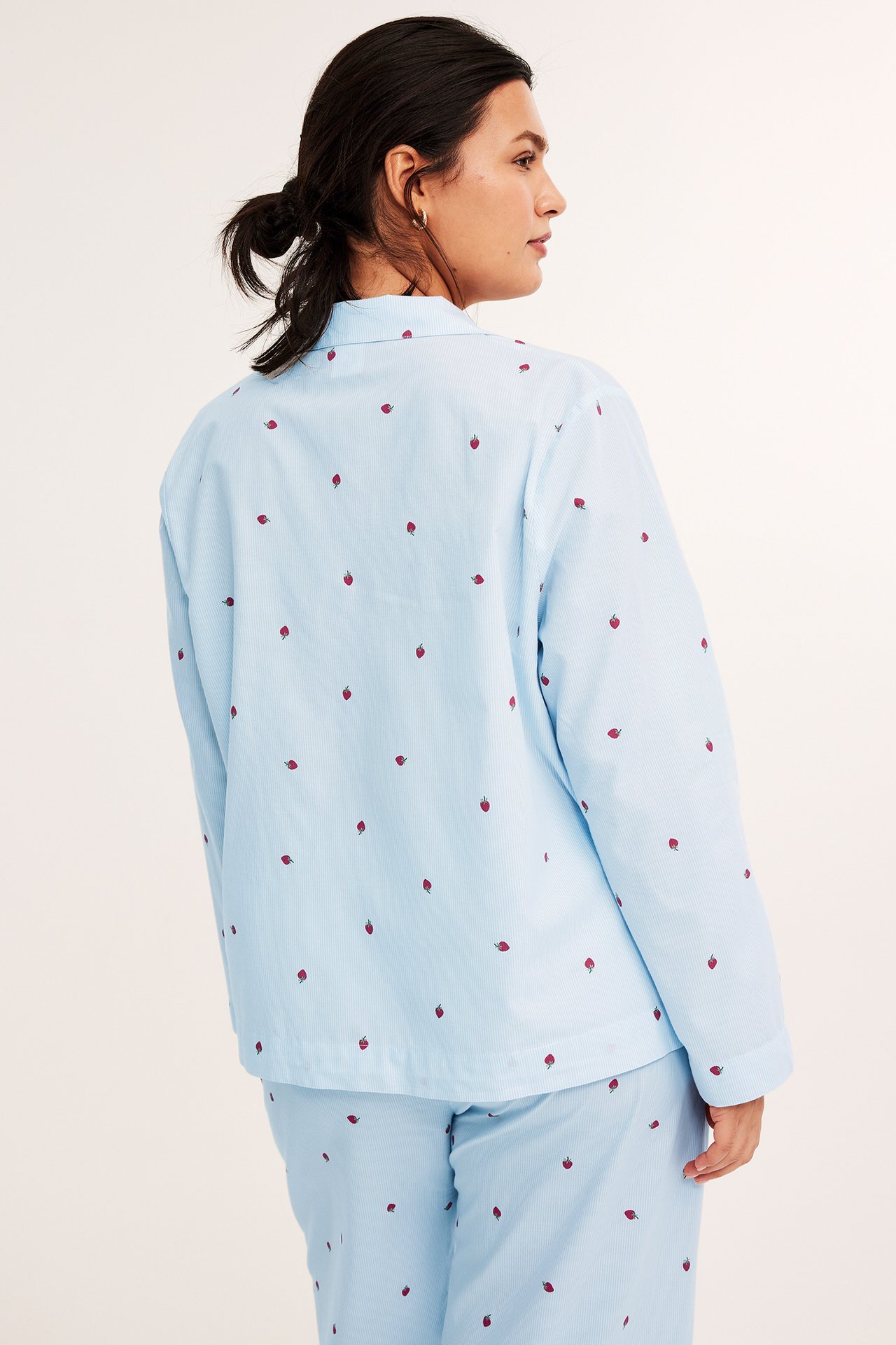 Naisen selkäkuva vaaleansinisessä puuvillapyjamapaidassa, jossa punainen mansikkakuvio ja yhteensopivat housut.