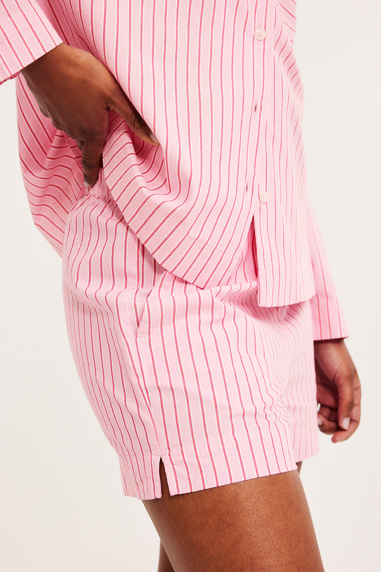 Sidovy av en kvinna i rosa randiga pyjamasshorts i bomull med resår och matchande skjorta.