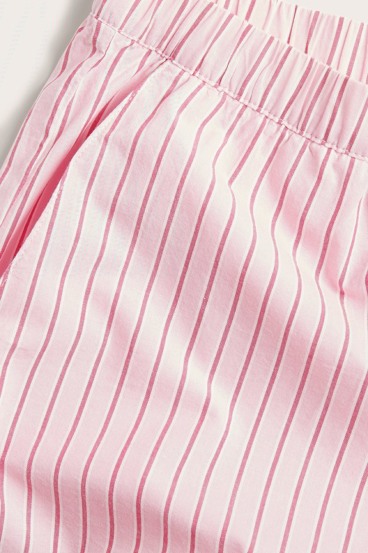 Zbliżenie różowo-białych, pasiastych, tkanych bawełnianych szortów piżamowych z elastyczną talią i kieszeniami.