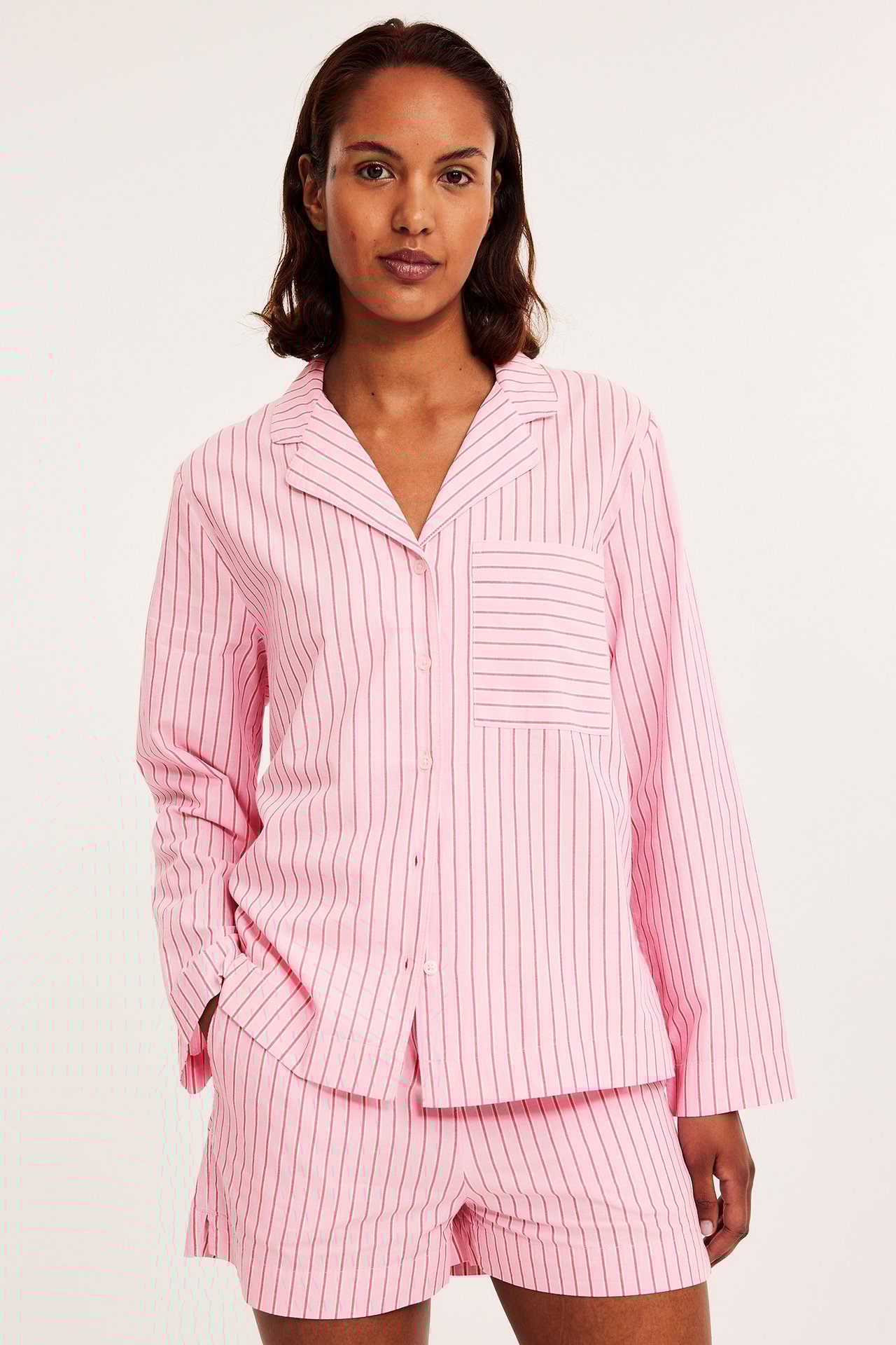 Widok z przodu: kobieta w różowej, pasiastym bawełnianej piżamie z szortami i koszulą z długim rękawem.