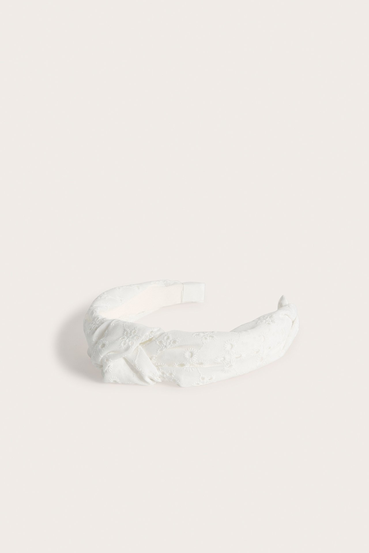 Närbild av ett vitt diadem med broderie anglaise och en knuten detalj.