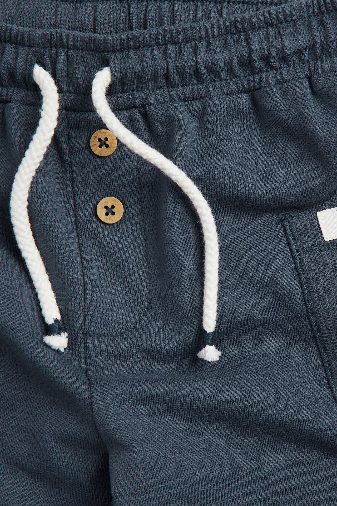 Nærbilde av mørkeblå bomullsshorts med elastisk midje, hvit snøring og dekorative treknapper.